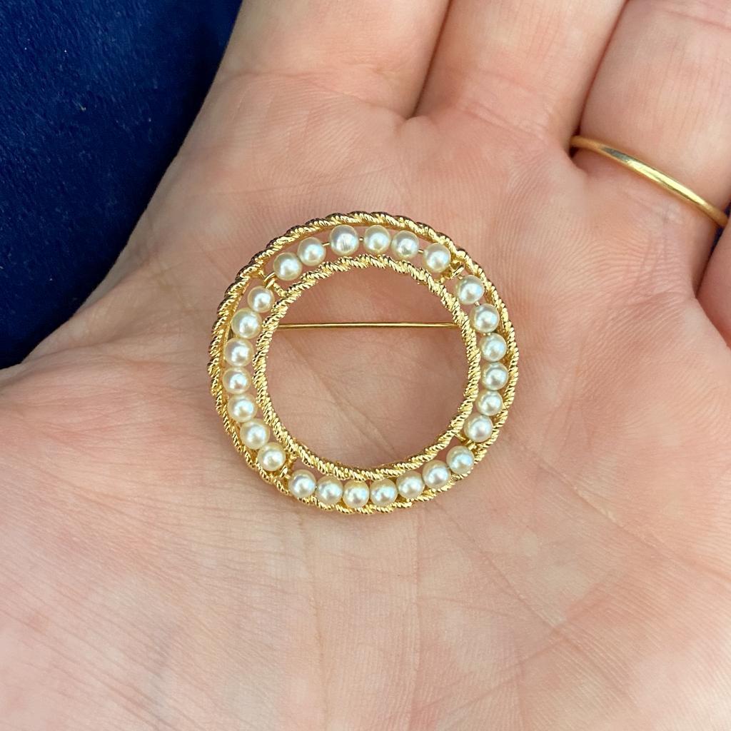 This is a beautiful freshwater pearl brooch with a lovely twisted rope 14 karat yellow gold double circle frame design. 26 small freshwater pearls are threaded on gold wire inside the frame. This pearl circle brooch is quite fine and a lovely accent