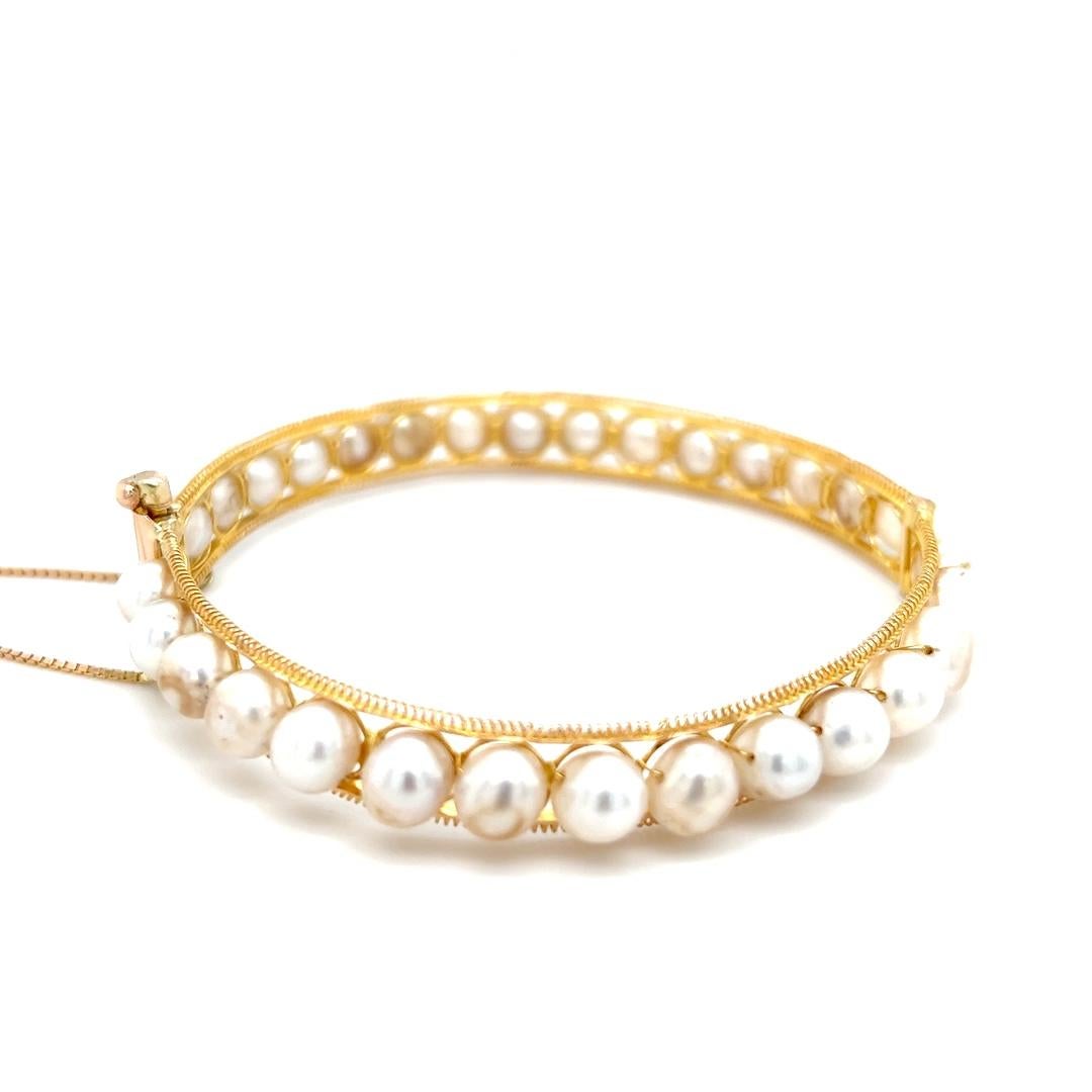 One 14 karat yellow gold hinged bangle bracelet set with thirty (30) ringed potato cream toned freshwater cultured pearls measuring between 7-8mm.  The bracelet measures 2.75 inches in diameter, 9.93mm wide with a tight pin lock and box change