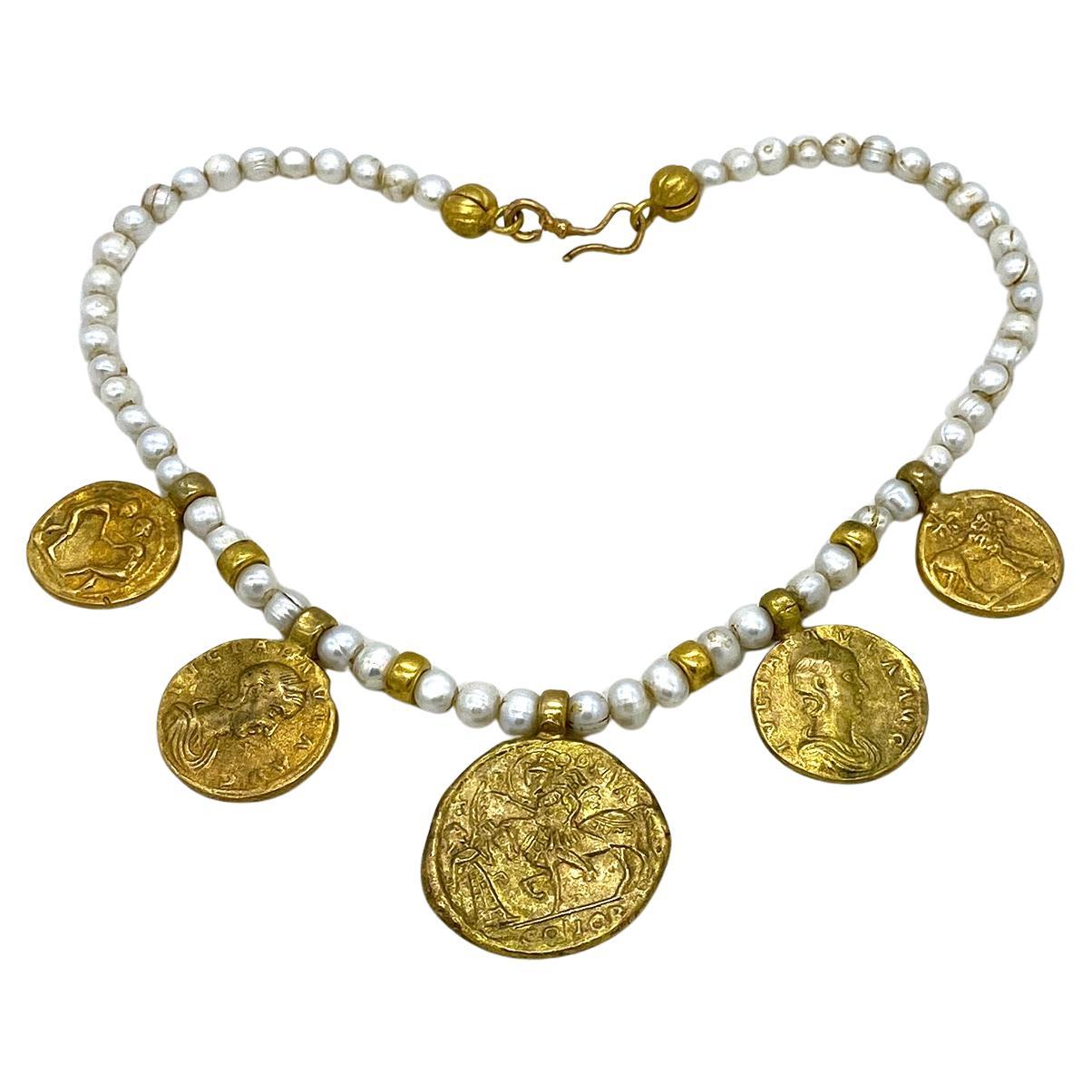 Il s'agit d'un collier de perles d'eau douce avec des charms en forme de pièces de monnaie romaines. Il est composé de perles baroques de 8 mm et d'éléments en bronze doré. Il y a cinq pièces de monnaie anciennes reproduites en dorure, de trois