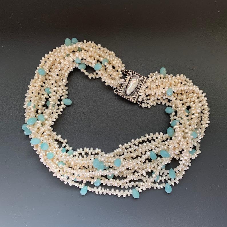 Stunning choker necklace is a true statement piece, featuring a beautiful torsade design crafted from sterling silver, faceted teardrop-shaped aqua gemstones, and lustrous freshwater pearls. Signed 925 KH, this necklace is a high-quality, designer