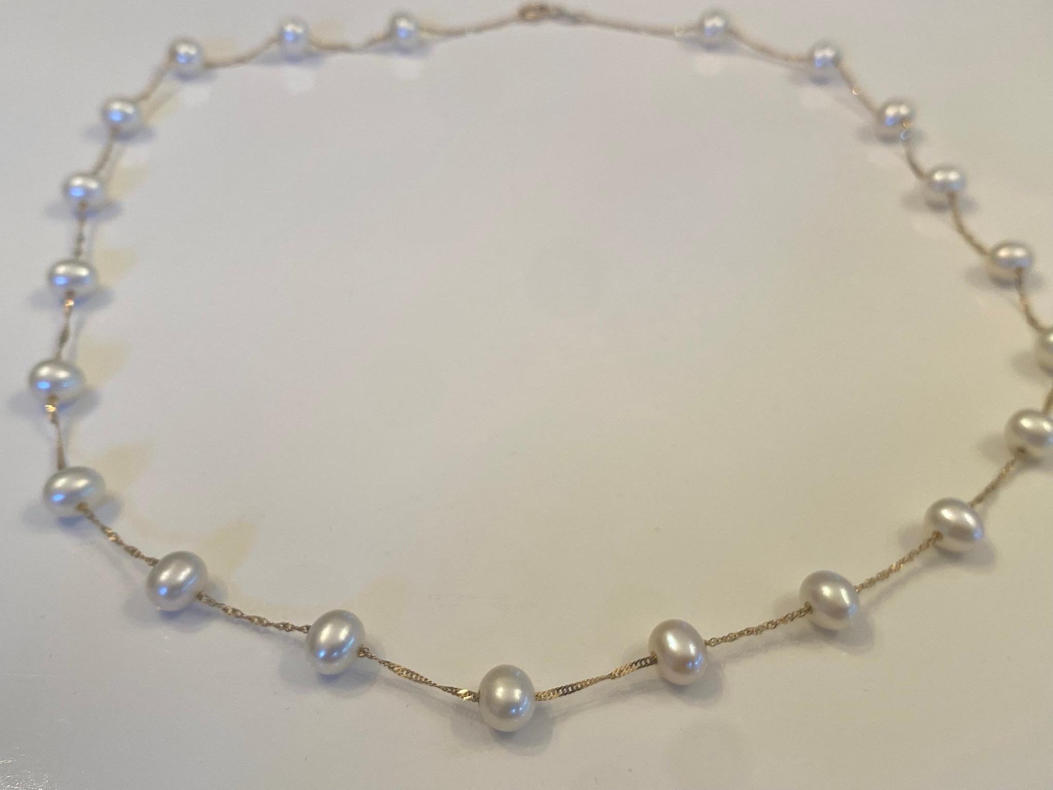 Ce délicat collier en or jaune 14 carats est composé de vingt-et-une perles blanches d'eau douce mesurant chacune environ 6 mm x 6,5 mm. Le collier mesure 18 pouces de long. 
