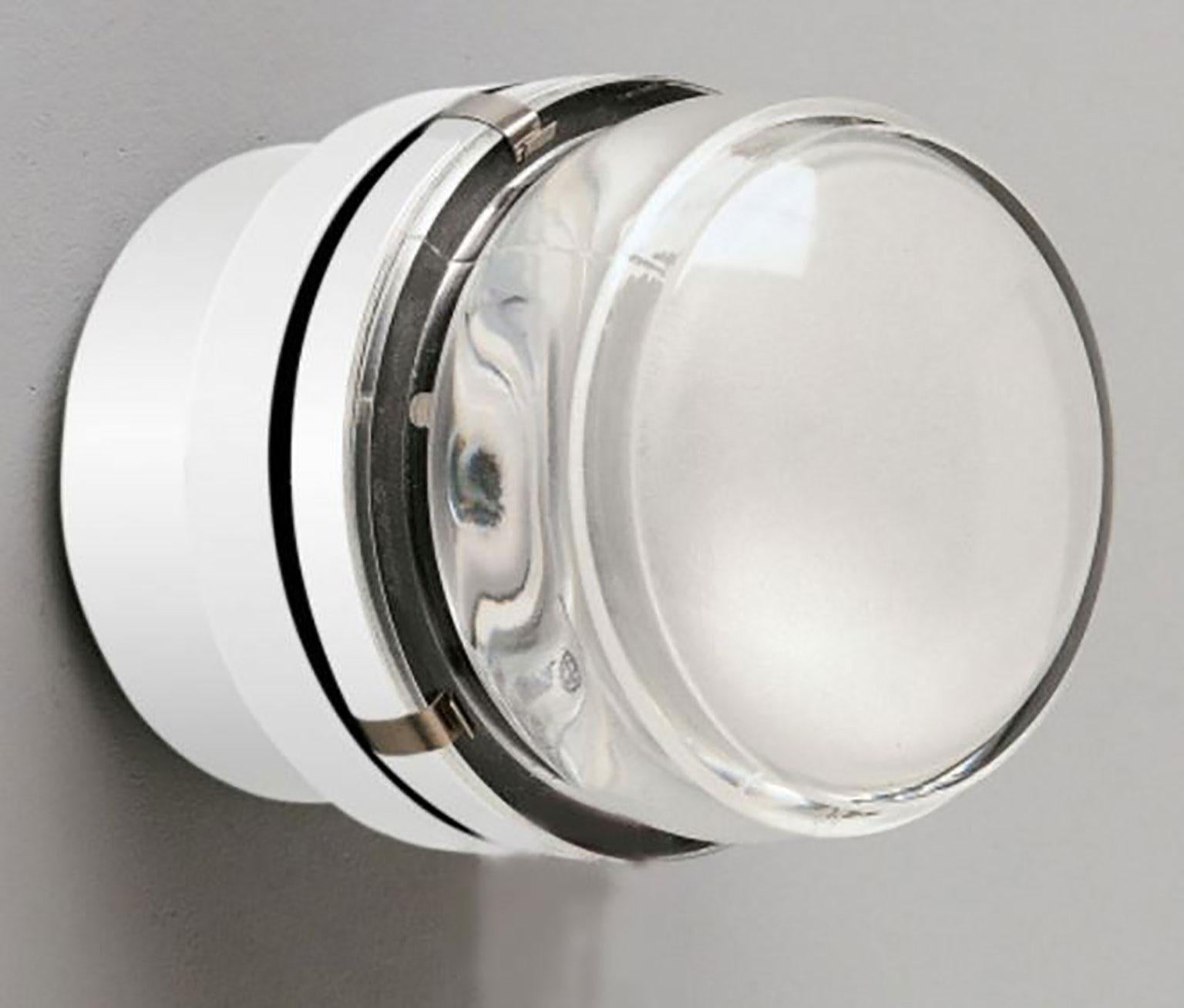 Applique Fresnel conçue par Joe Colombo pour Oluce. Simple et intemporelle, cette lampe produit à la fois une lumière directe et diffuse. L'appareil est fabriqué en aluminium chromé. La lentille de la lampe est en verre de haute qualité. Disponible