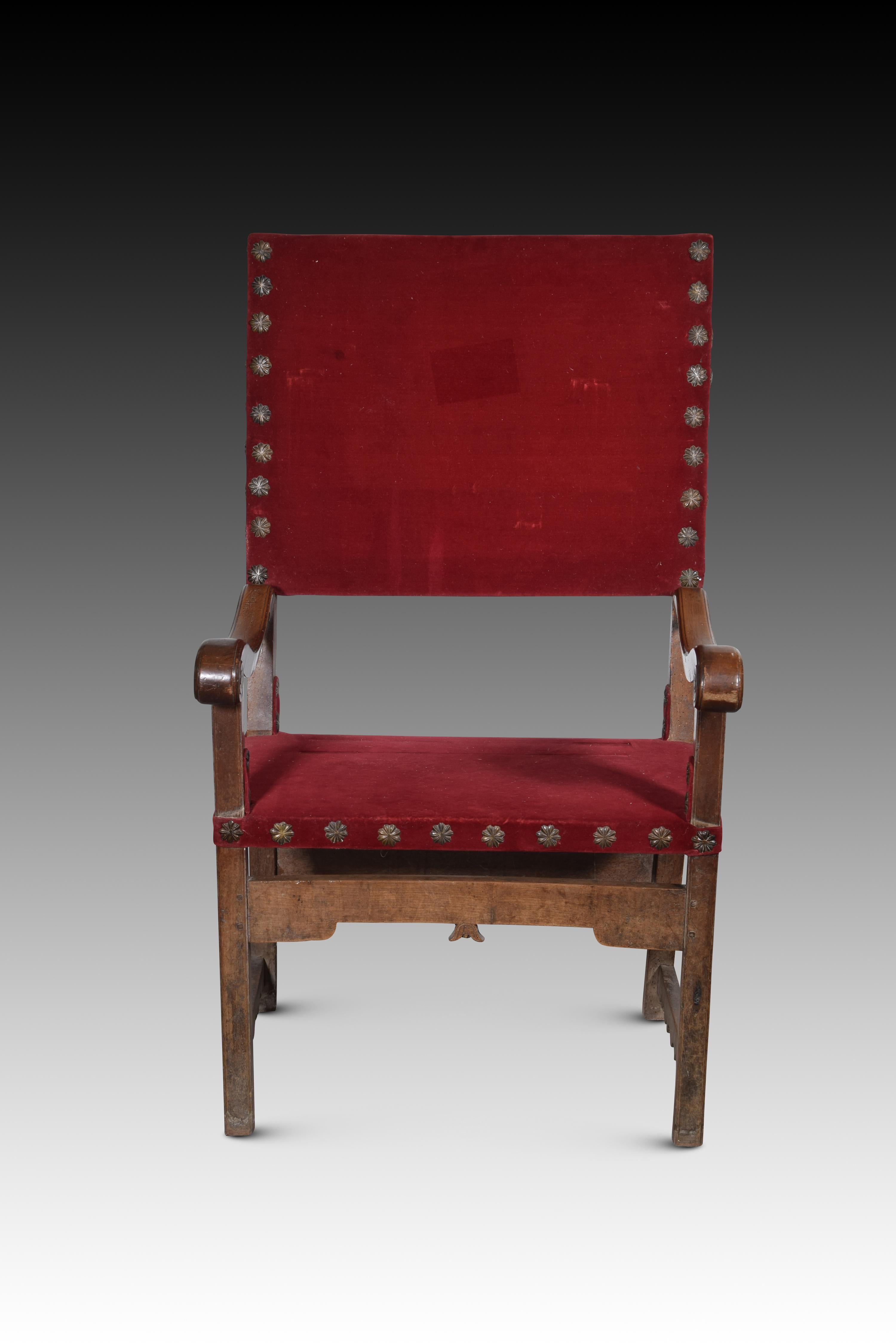 Friar armchair. Walnut wood, textile. Spain, 17th century. 
Armchair with arms and high back of the type known as “frailero”, which has a textile upholstery with studs on the seat and back, low cut-out low profile chambrances joining the front legs