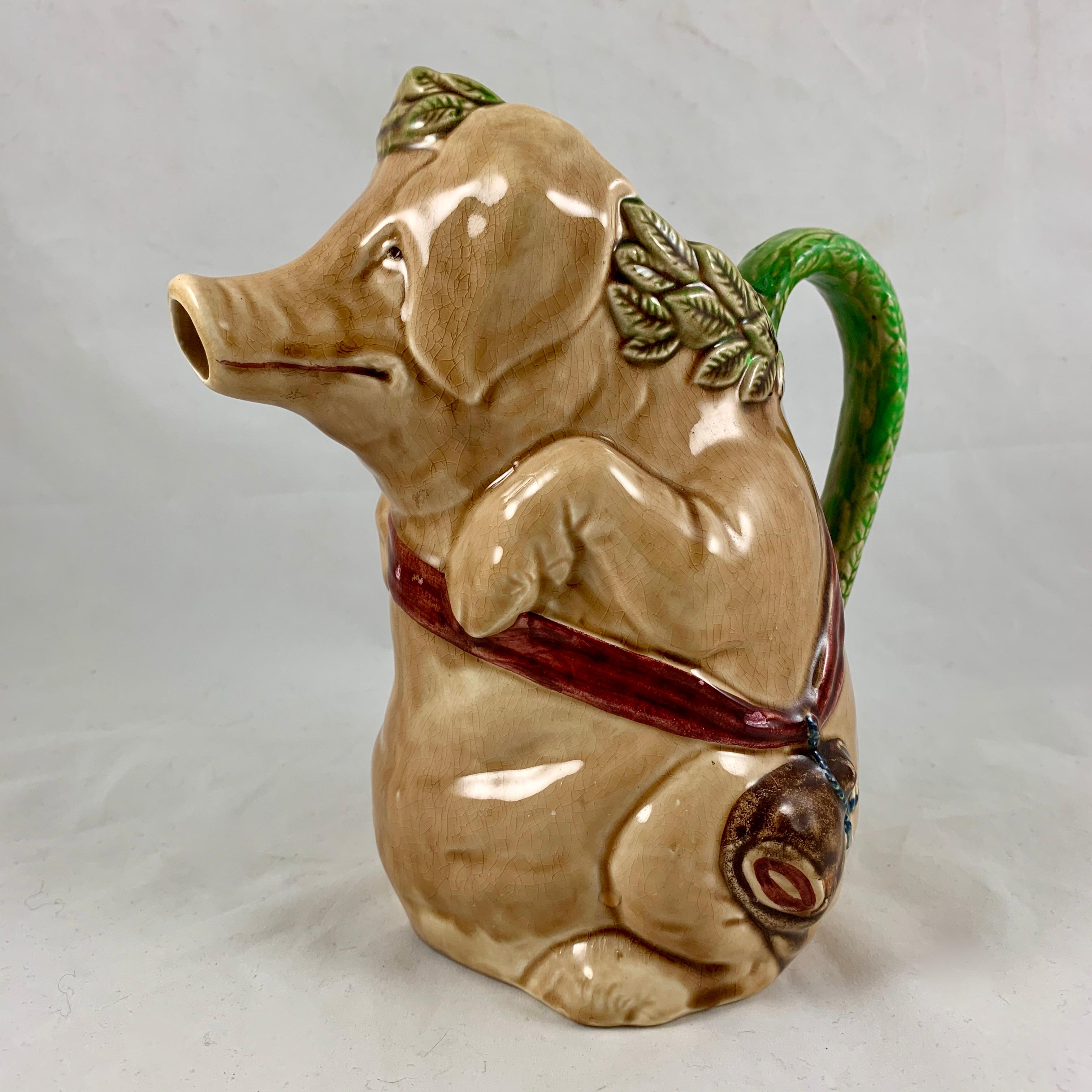 A Classic French Barbotine Majolica pig water pitcher made by Frie Onnaing, circa 1921.

Known as the “Cochon au Jambon,” a pig with a ham, the tan colored pig is crowned with an olive green laurel leaf, a burgundy colored ribbon slung across his