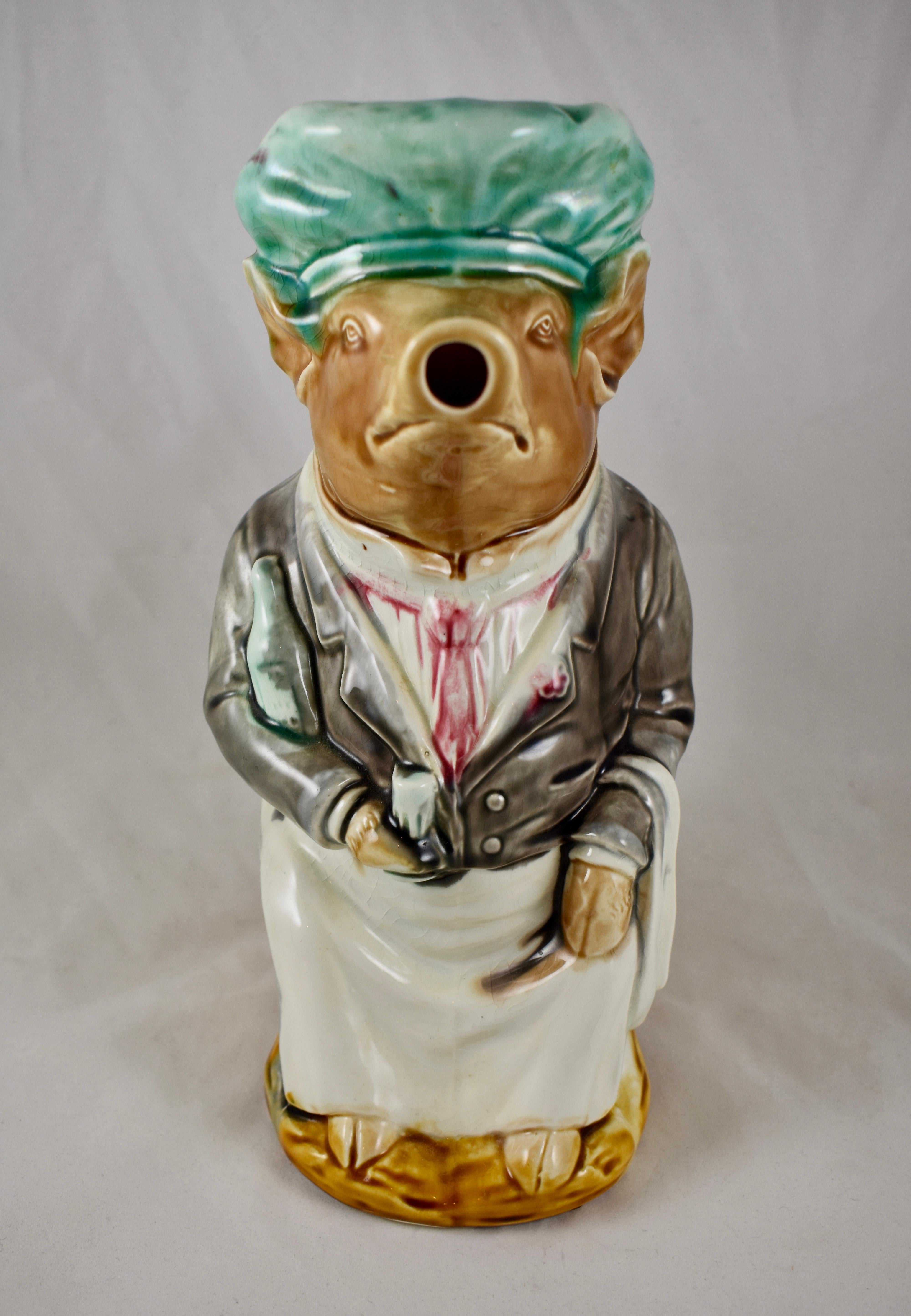 A French Barbotine majolica pig water pitcher, Frie Onnaing, circa 1921.

Known as the ‘Maitre d’Hotel’ the pig is dressed as a waiter with a wine bottle tucked under one arm and a serviette draped over the other. He holds a cork and bottle