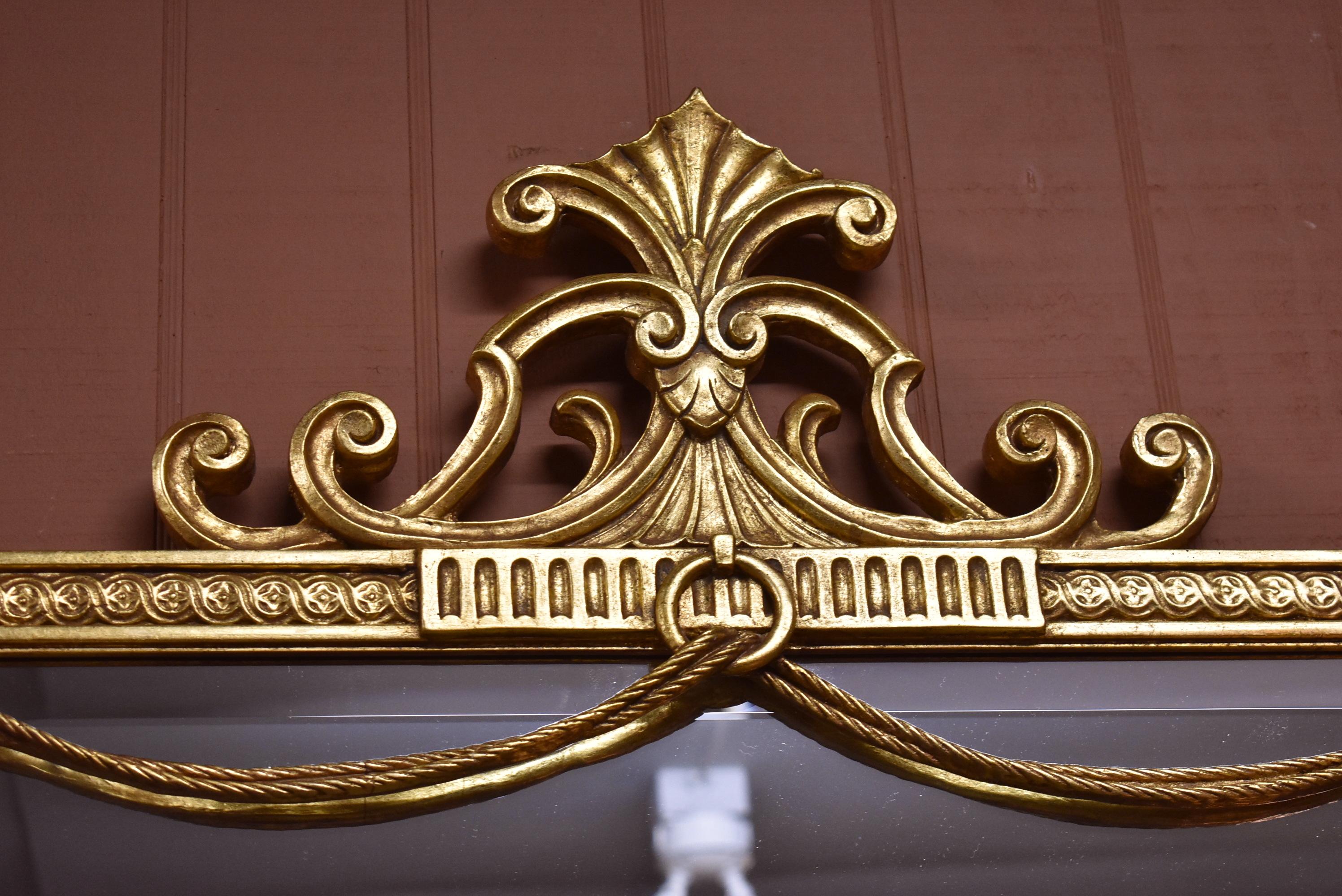 Friedman Brothers carved French style gilt beveled mirror. Two figural lion heads flank top corners. Tasseled rope swags across the top under carved center plume pediment.