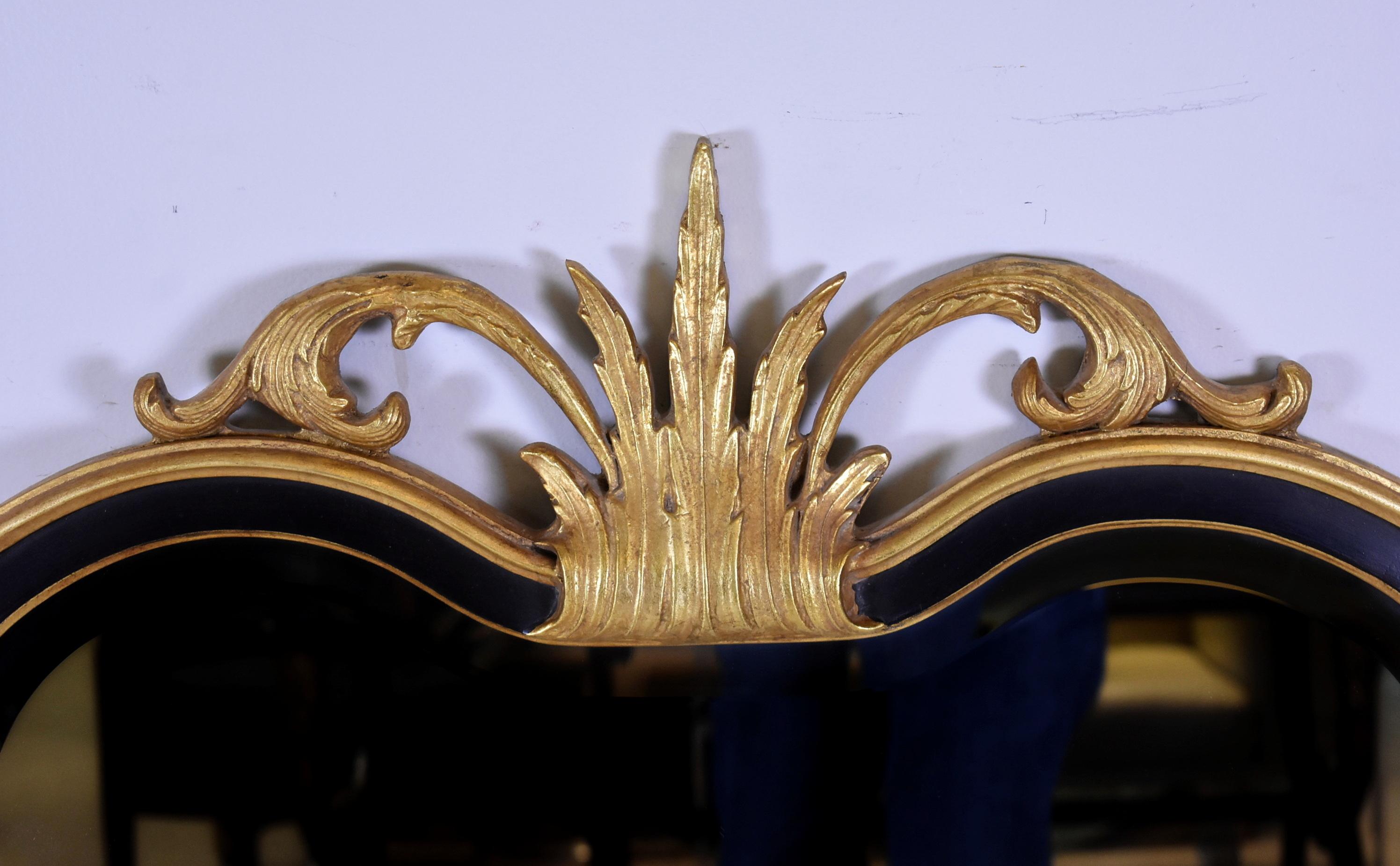Specchio da parete di Friedman Brothers con cornice in legno dorato intagliato nero e oro con un disegno di foglie e volute sulla parte superiore e vetro smussato. Larghezza 28 1/2