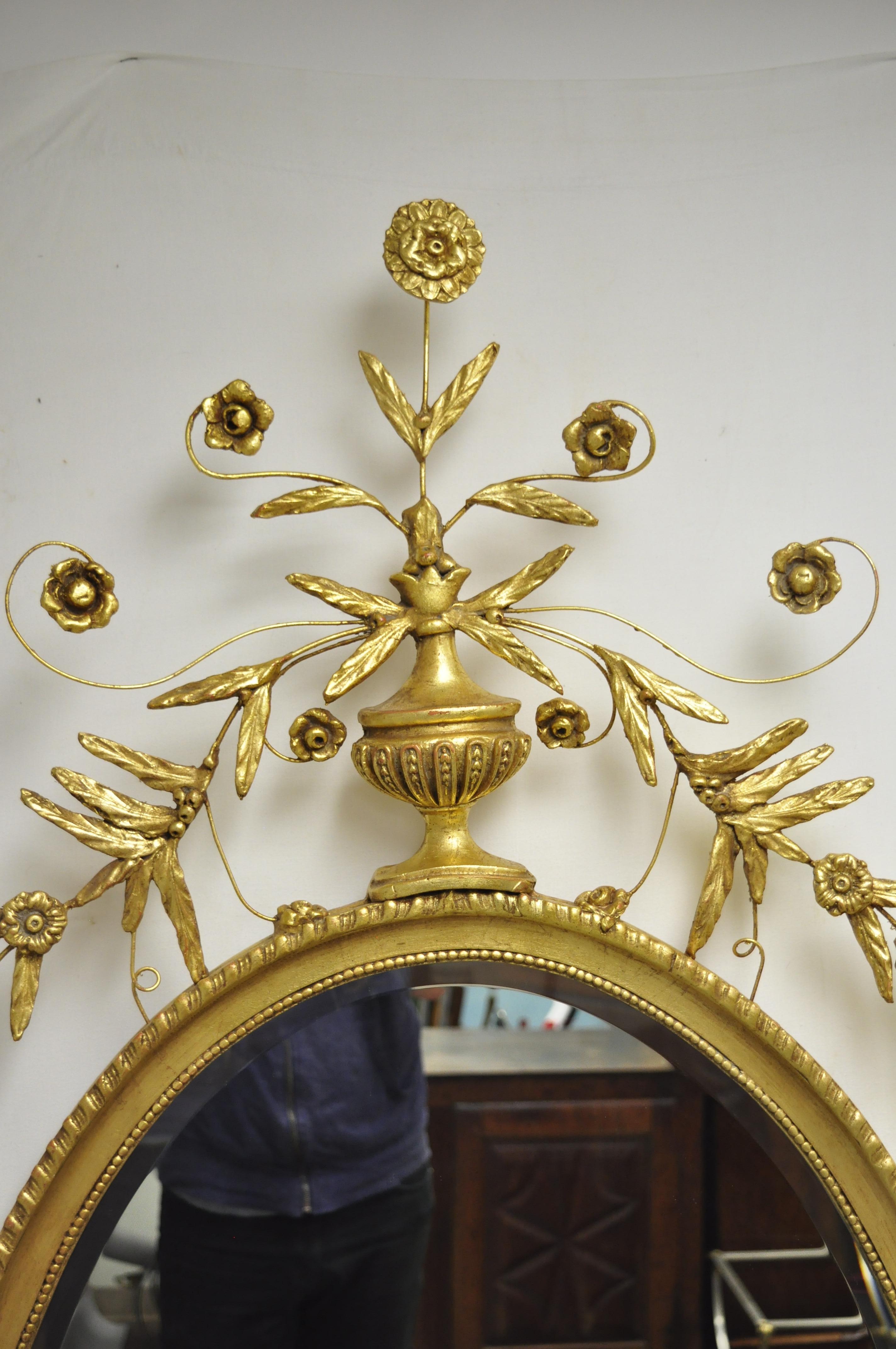 Friedman Brothers grand miroir mural ovale en bois doré de style Adams. L'article présente une urne et une couronne de feuilles, un cadre doré, une étiquette originale, un verre ovale biseauté, un style et une forme remarquables, vers le 20e-21e