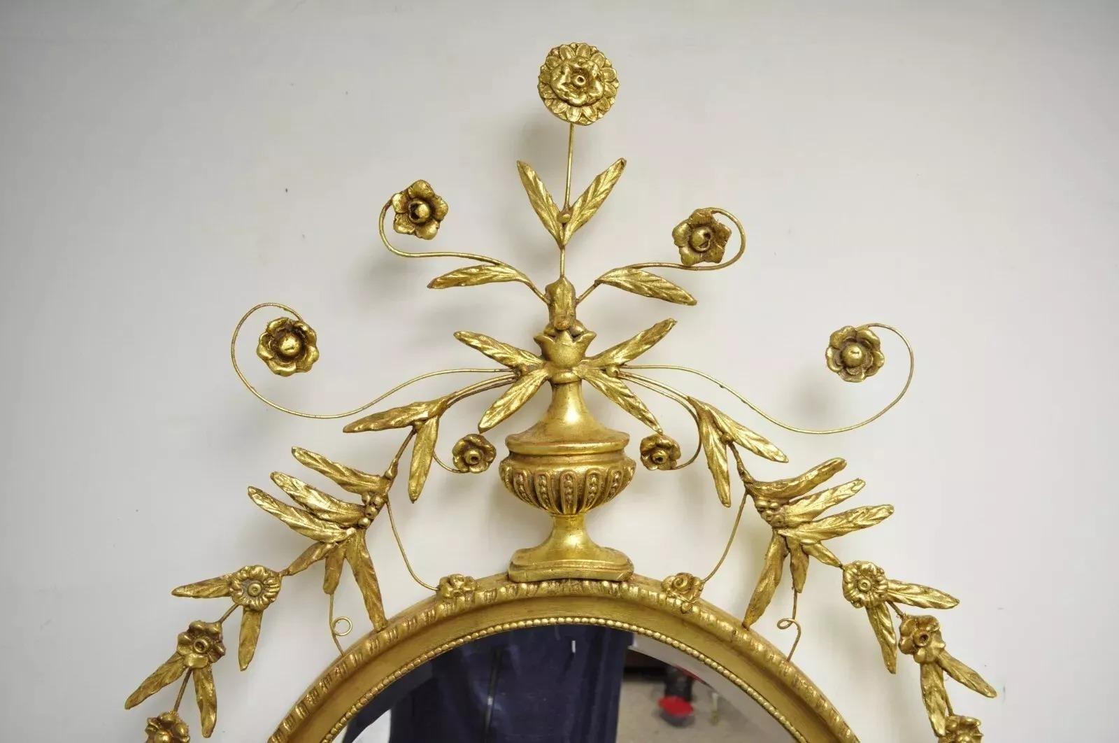 Specchio da parete ovale di grandi dimensioni in stile Adams con legno dorato di Friedman Brothers. L'articolo presenta un'urna e una corona di foglie, una cornice dorata, un'etichetta originale, un vetro ovale smussato, uno stile e una forma