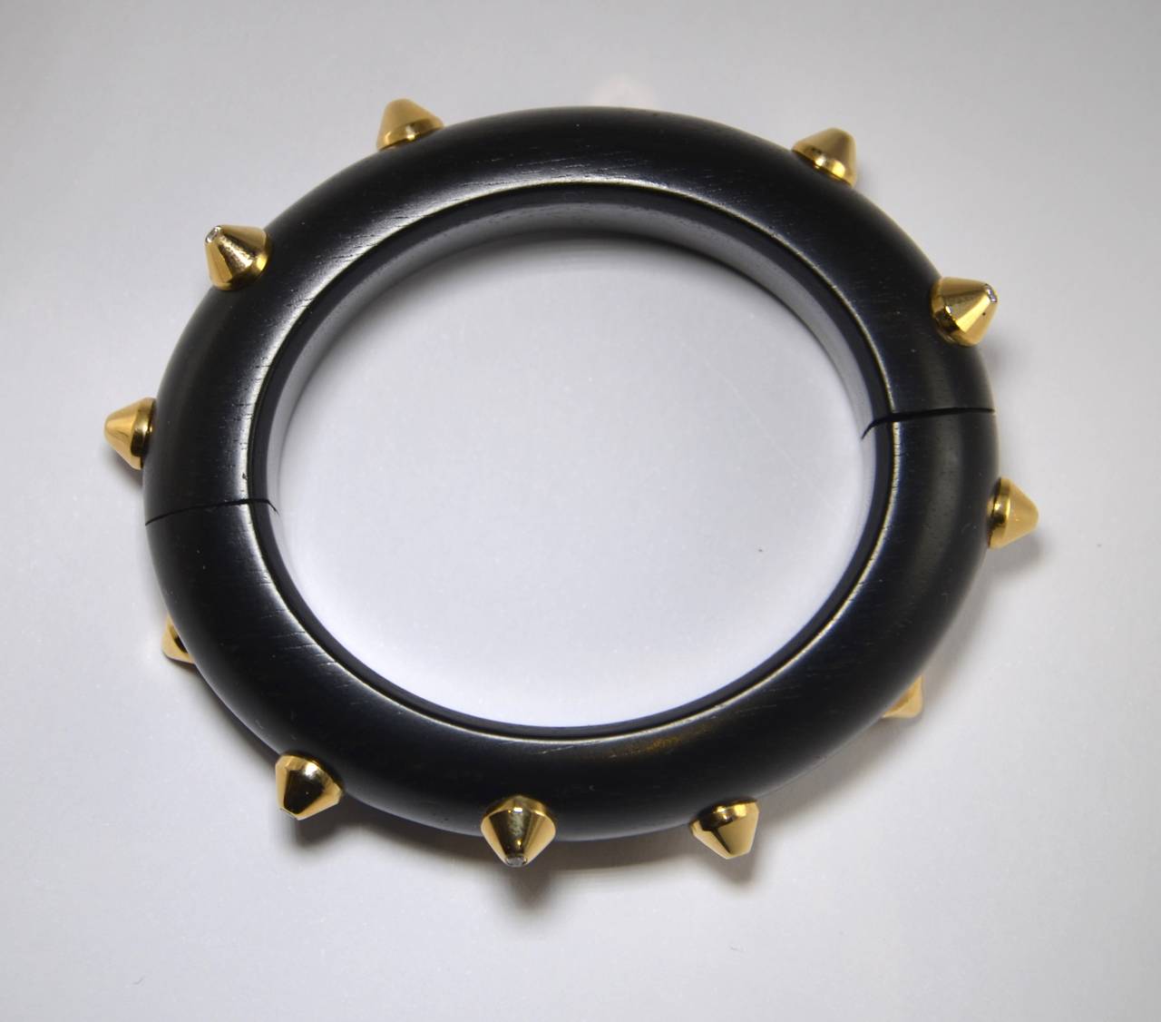 Ebony Wood Bangle with 12 Pyramids made of 18 KT Yellow Gold topped with a Diamond. The closing device is rotatably mounted in the sides. 

Brillant Cut Diamonds of approx. 0.41 ct., TW/vvs

Inside Dimension 54 x 47 mm, oval shape