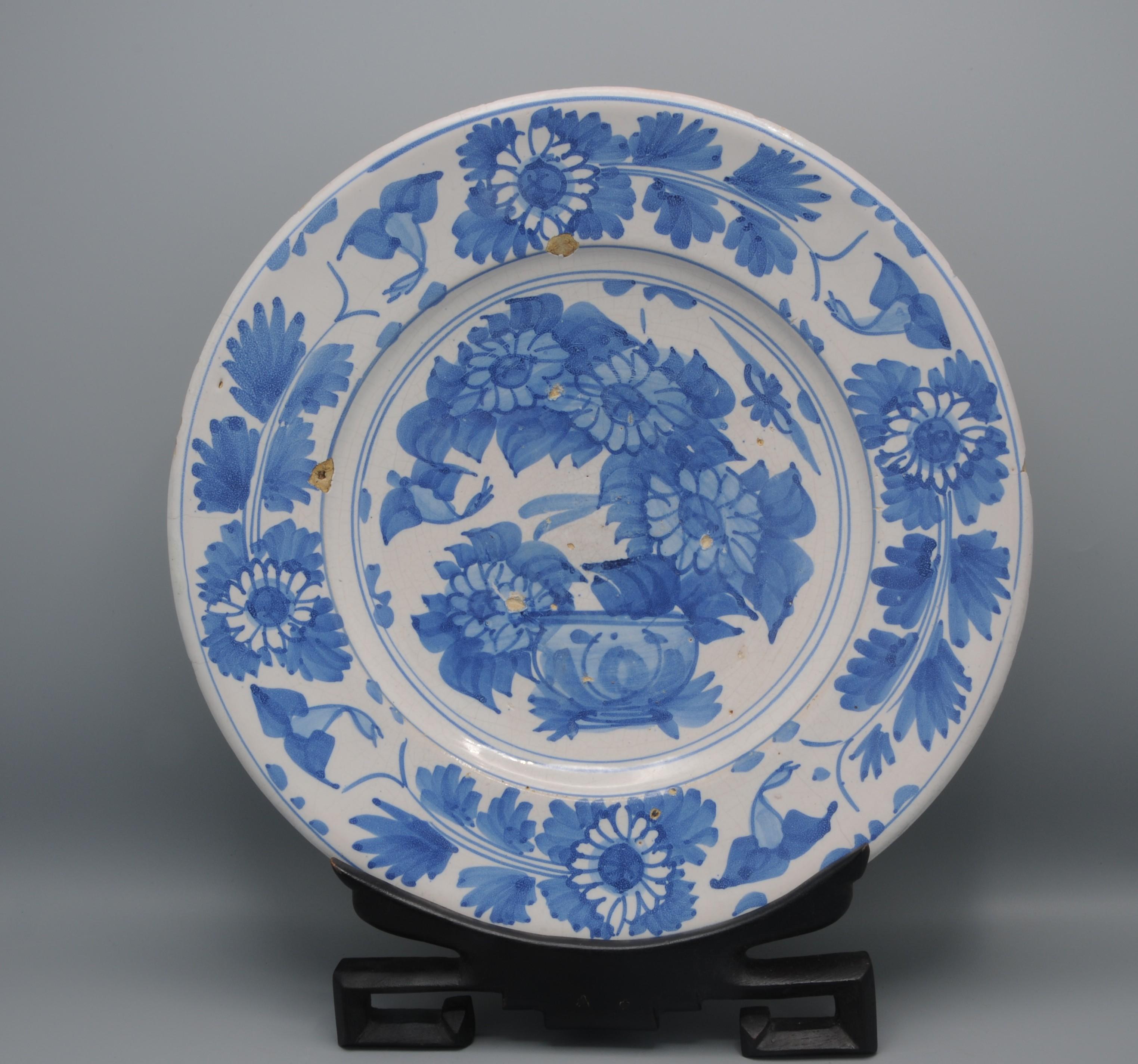 Il piatto ha un bordo ampio e dolcemente inclinato ed è decorato in blu con una composizione floreale liberamente dipinta in un vaso al centro, racchiuso in un doppio cerchio. Il bordo è riccamente ornato da fiori e foglie dipinti a mano, applicati