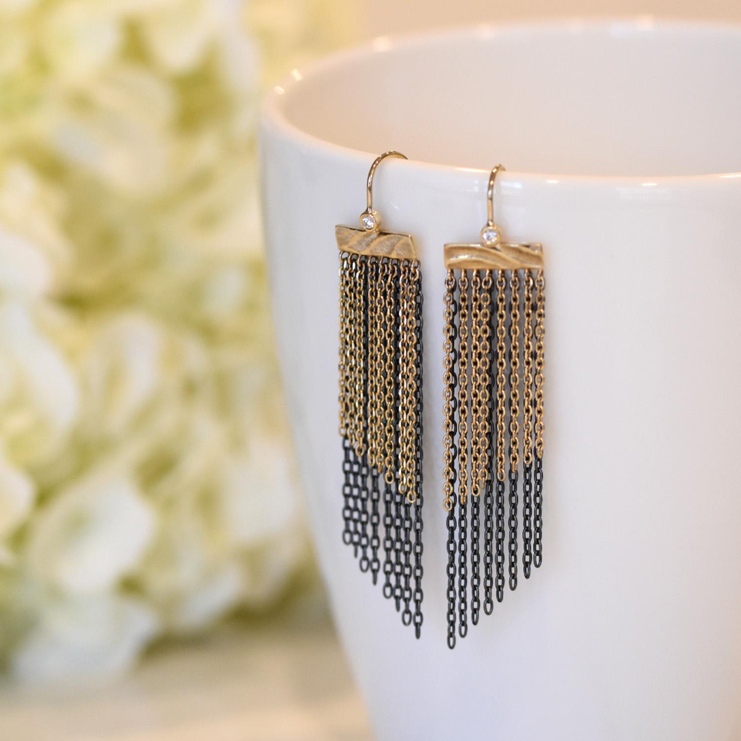 K.Mita's Shoreline Fringe Earrings depict ocean waves streaming through sand along the shore. The double layer of oxidized sterling silver and 14 karat yellow gold chains are constantly in motion shifting the pattern and reflecting light similar to