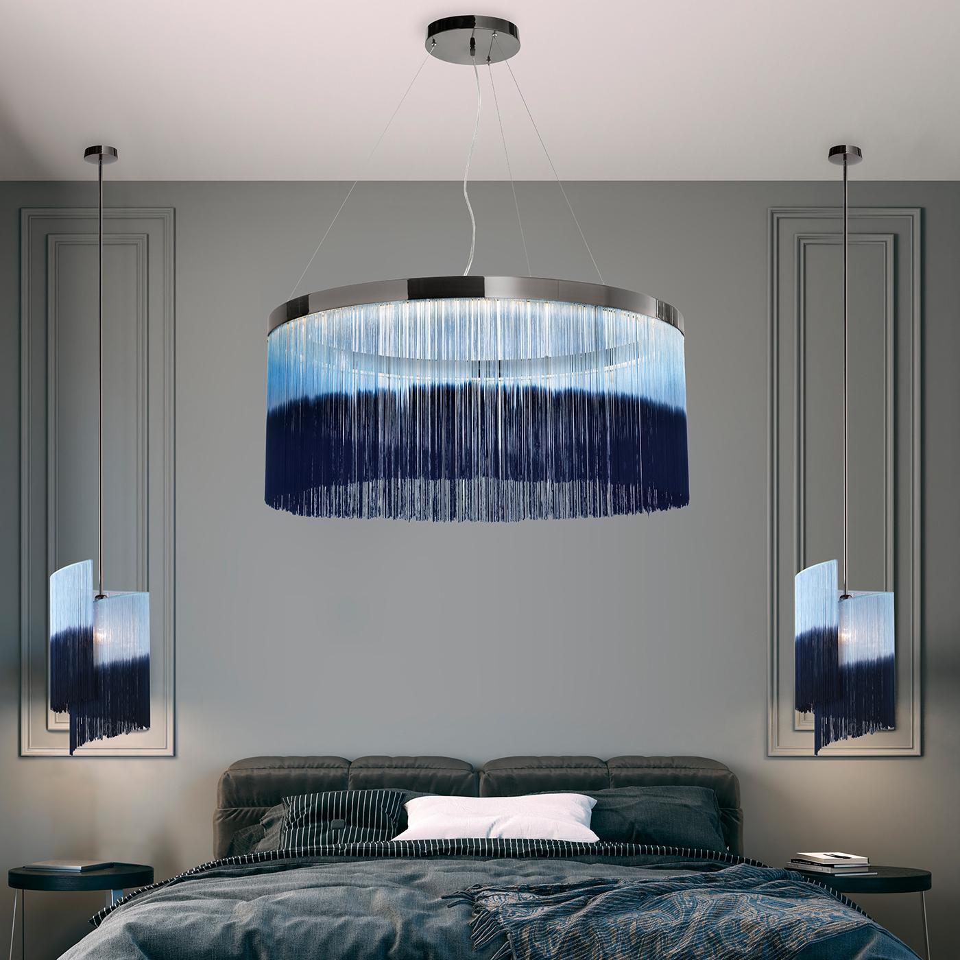 A statement of glamour and tailored character will imbue contemporary bedrooms or living rooms with the display of this luxe chandelier. A myriad of fringes hand-dyed in two contrasting tones of blue dangles from the glowing metal ring that hosts