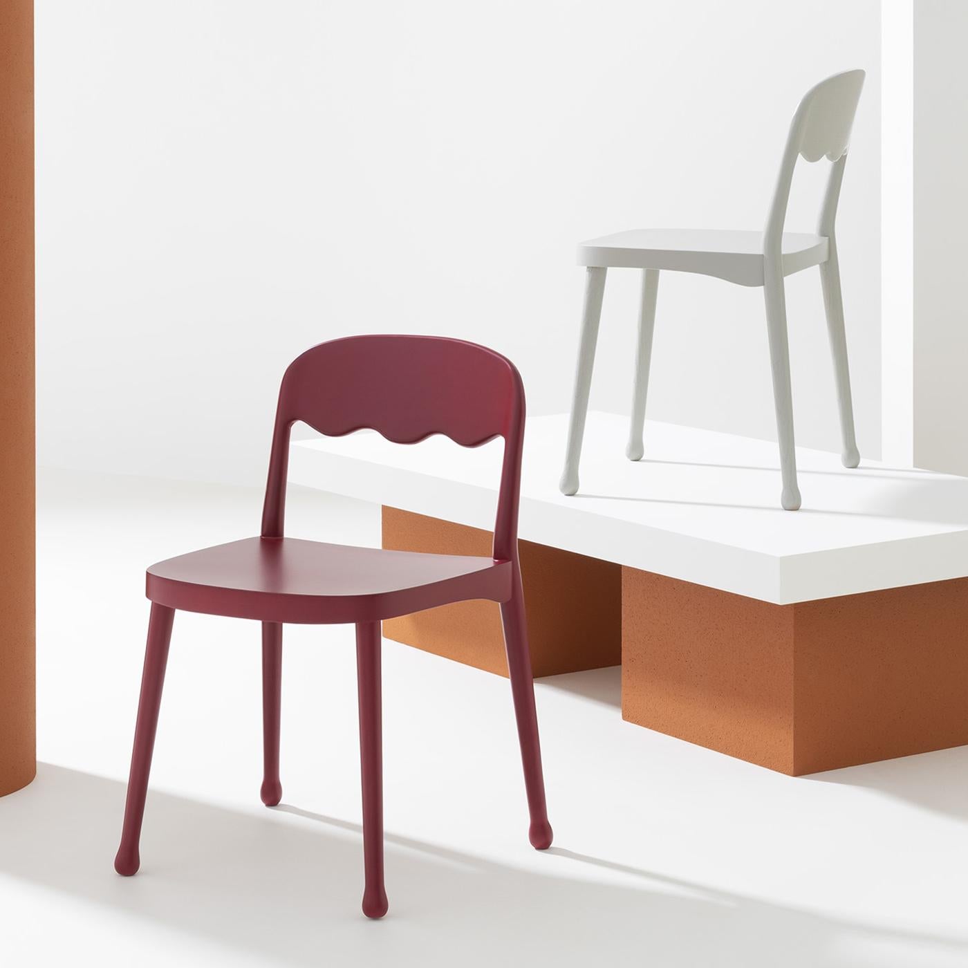 Elegant and ergonomic, this splendid design by Cristina Celestino will make a bold statement in a modern decor. Fashioned of red-lacquered beechwood with a matte finish, this chair boasts a simple silhouette marked by an open and waved backrest and