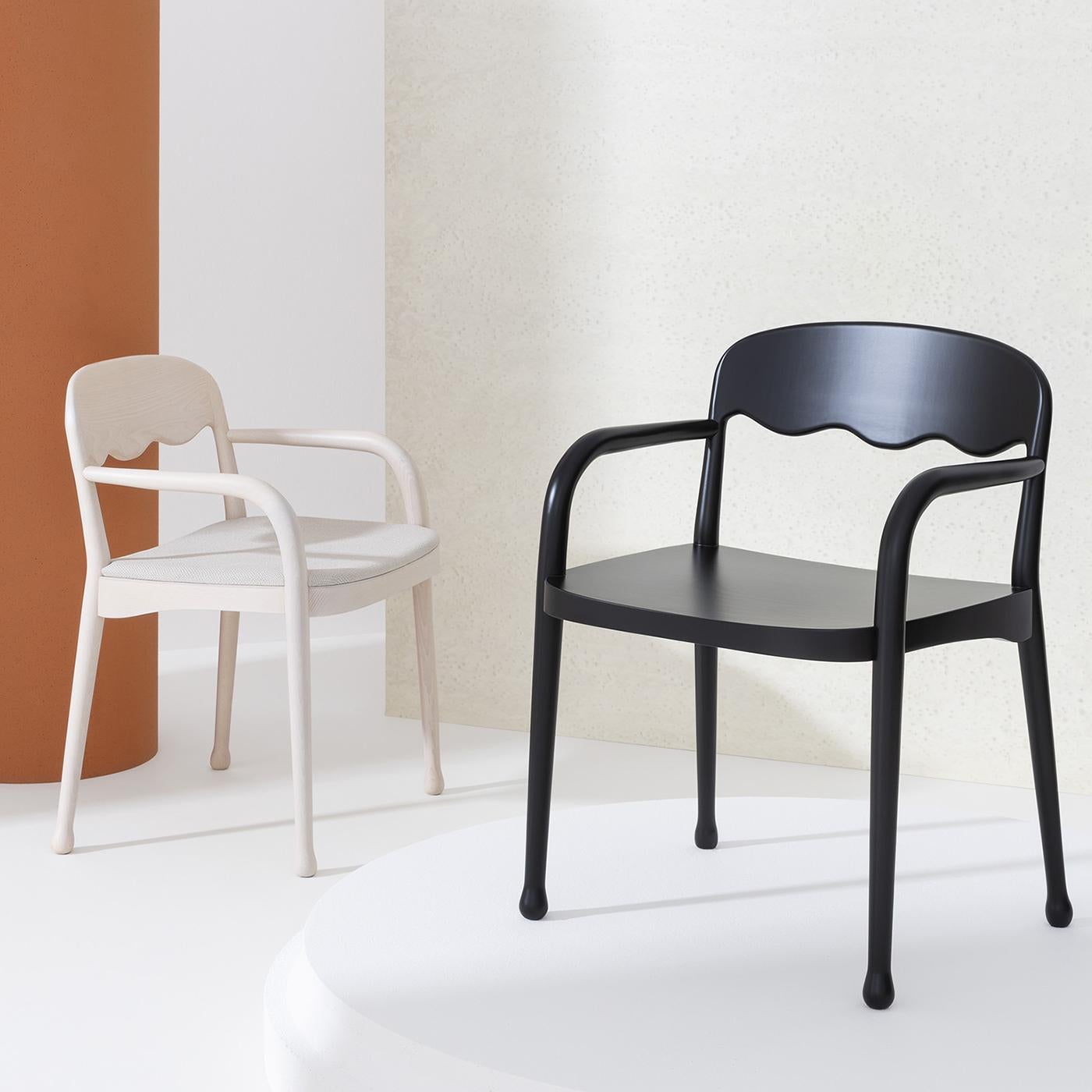 Boasting a total-black look with a matte finish, this armchair is a refined design by Cristina Celestino. Crafted of beechwood, its ergonomic seat rests on four slightly slanted legs completed with round feet and felt pads, and is embellished with a
