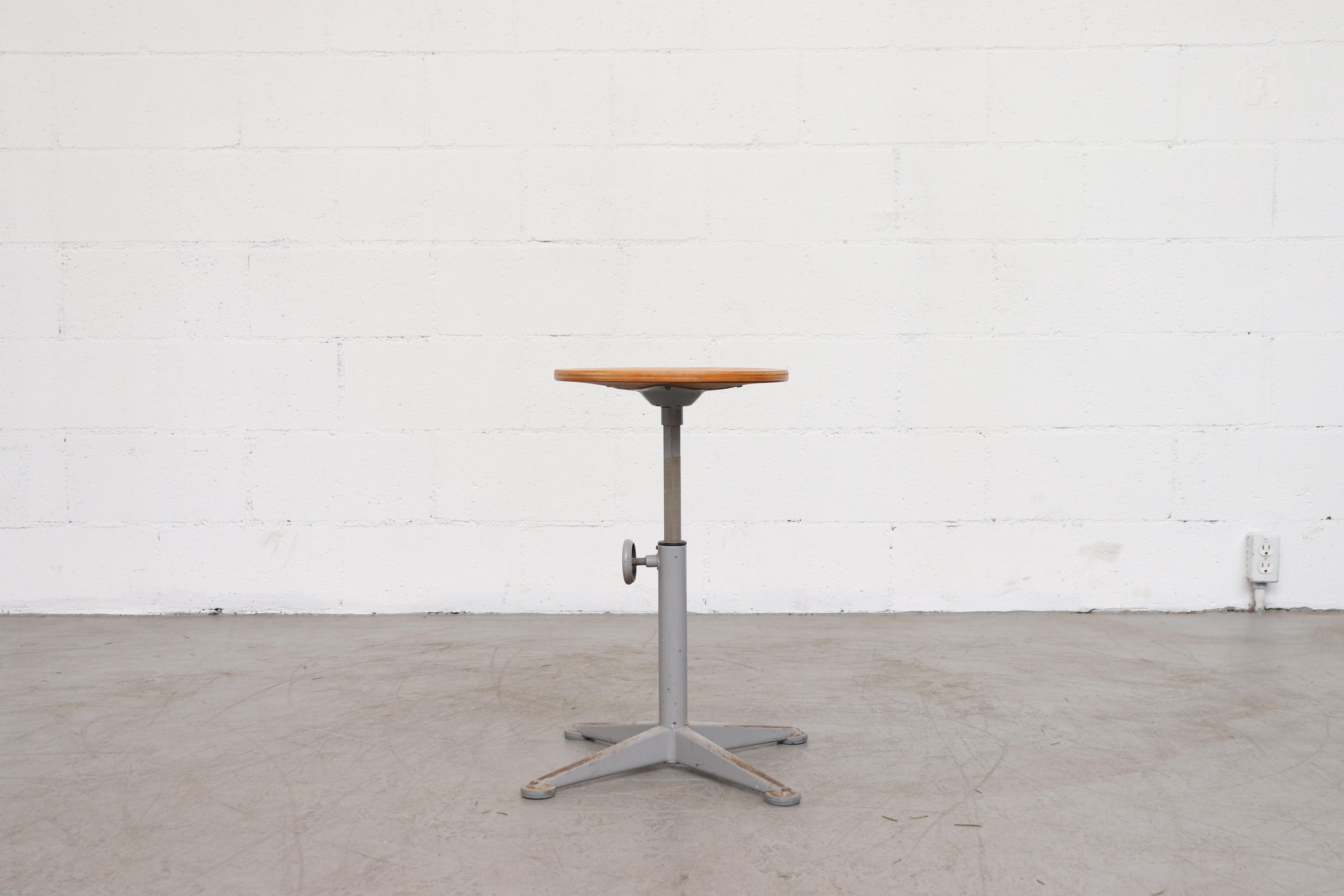 Backless drafting stool by Friso Kramer for Ahrend de Cirkel, plywood seat with small pedestal base. Adjustable height with original knob. Visible wear to the enamel and plywood. In original condition.