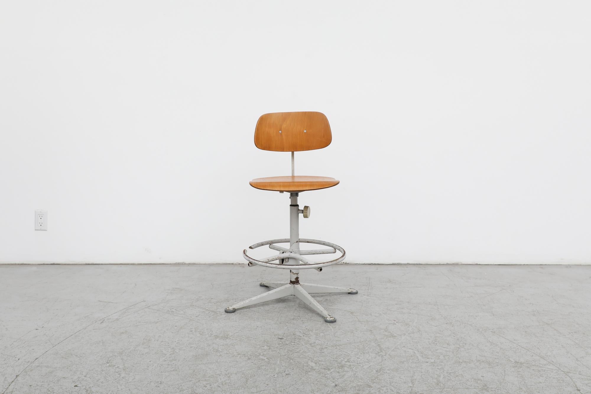 Authentic Friso Kramer designed industrial drafting stool for Dutch Mid-Century office furniture manufacturer Ahrend de Cirkel, circa 1950s. Grey enameled metal frame paired with a plywood seat and backrest. Height adjustable seat and footrest with