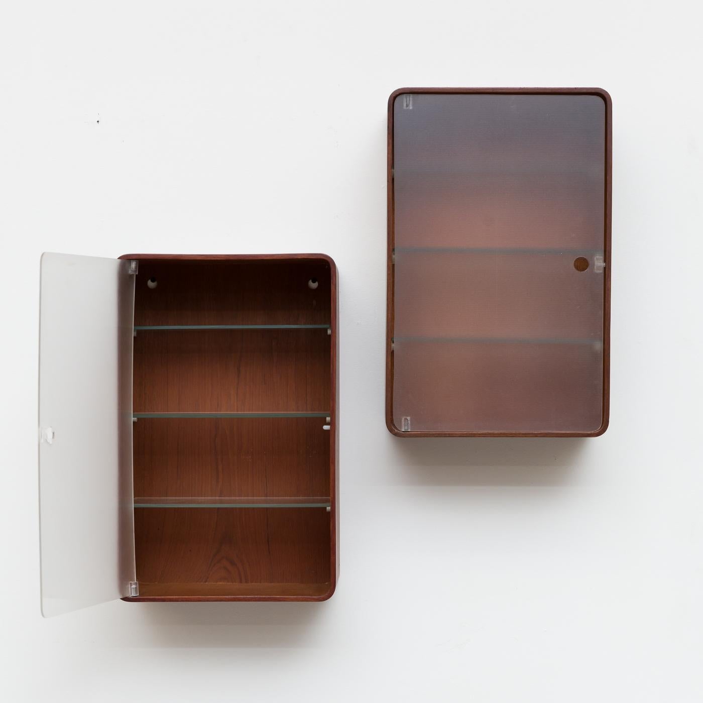 Rare midcentury wall mount medicine cabinet. Two available, slightly different wood colors. A= Reddish and B=Teak both have plexiglass doors with finger cutouts. Ribbed glass shelves inside. Very original condition, slight bowing to the doors, open
