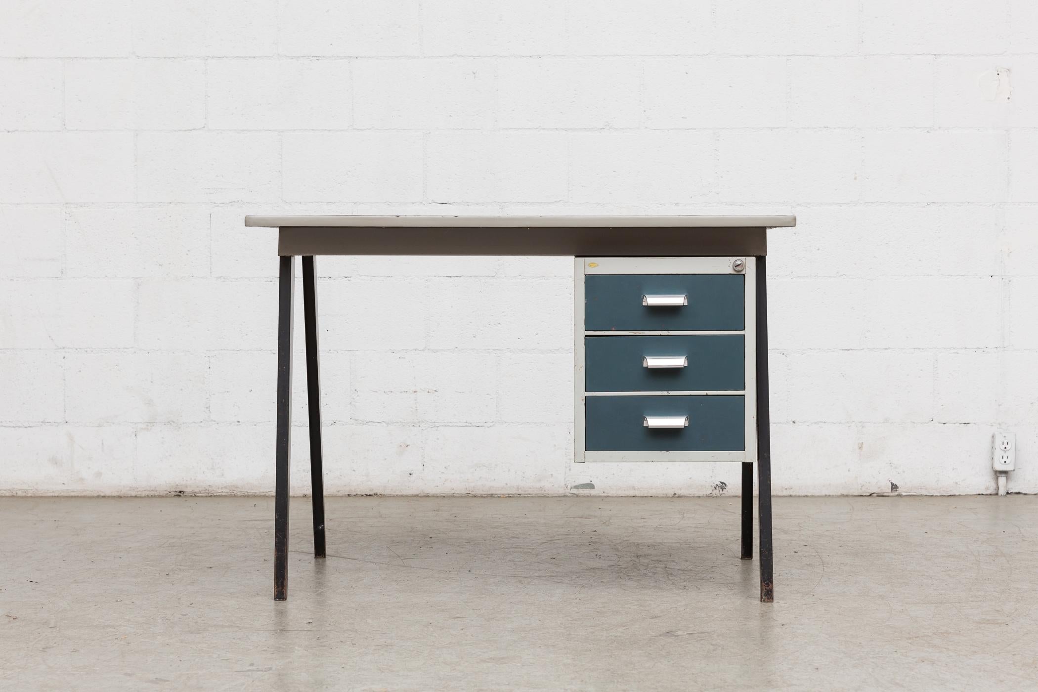 Midcentury industrial metal desk with blue-ish enameled metal drawers, light grey metal casing and black enameled metal Prouve style legs. Black linoleum top is well worn with visible wear, scratching, discoloration and indentation.