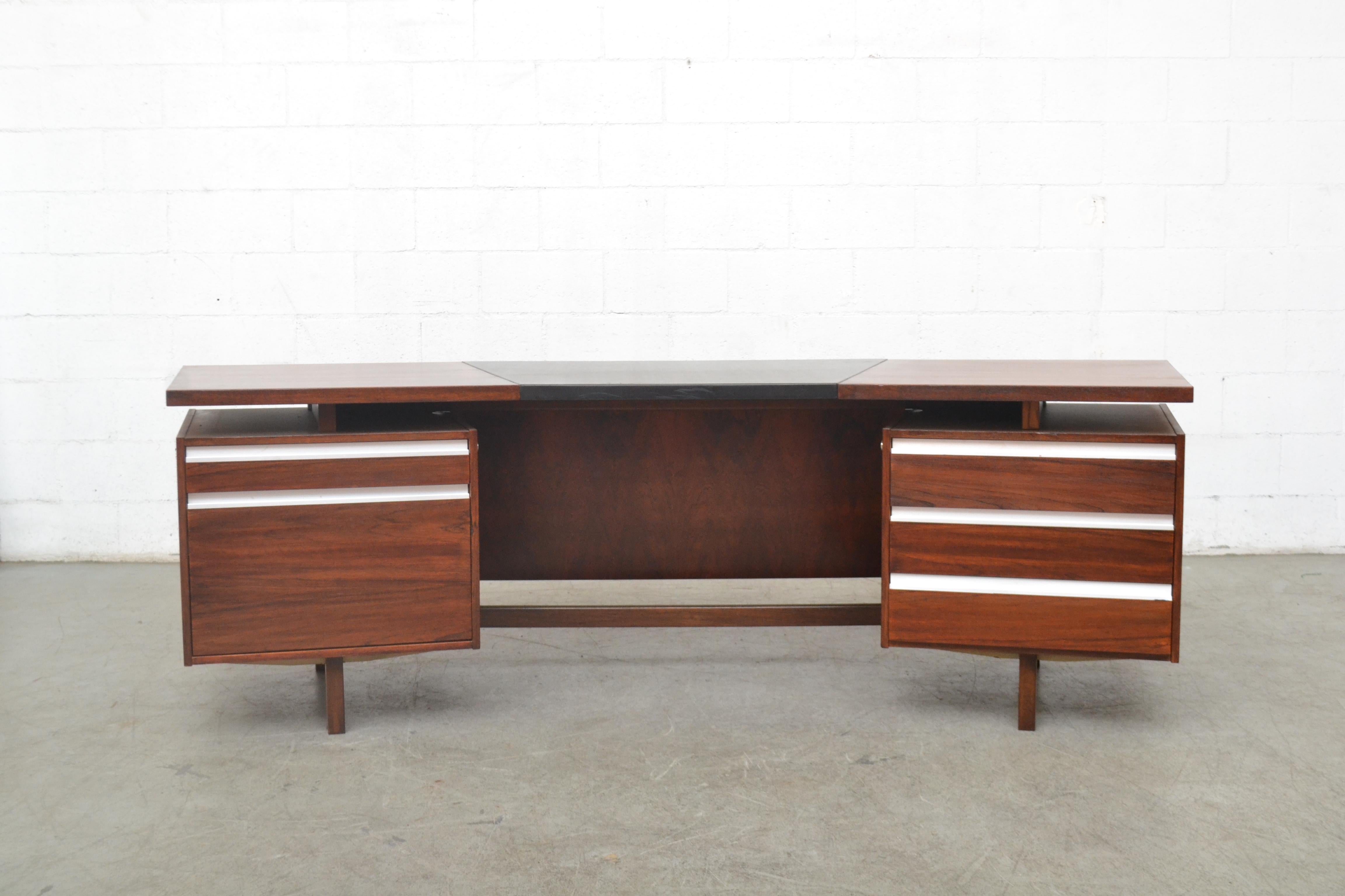 Impressive midcentury executive desk by Fristho. Lightly refinished rosewood with original black skai top. Visible wear and some scratches on the vinyl top. Right side has three sliding drawers and a filing cabinet and top drawer with sliding wood