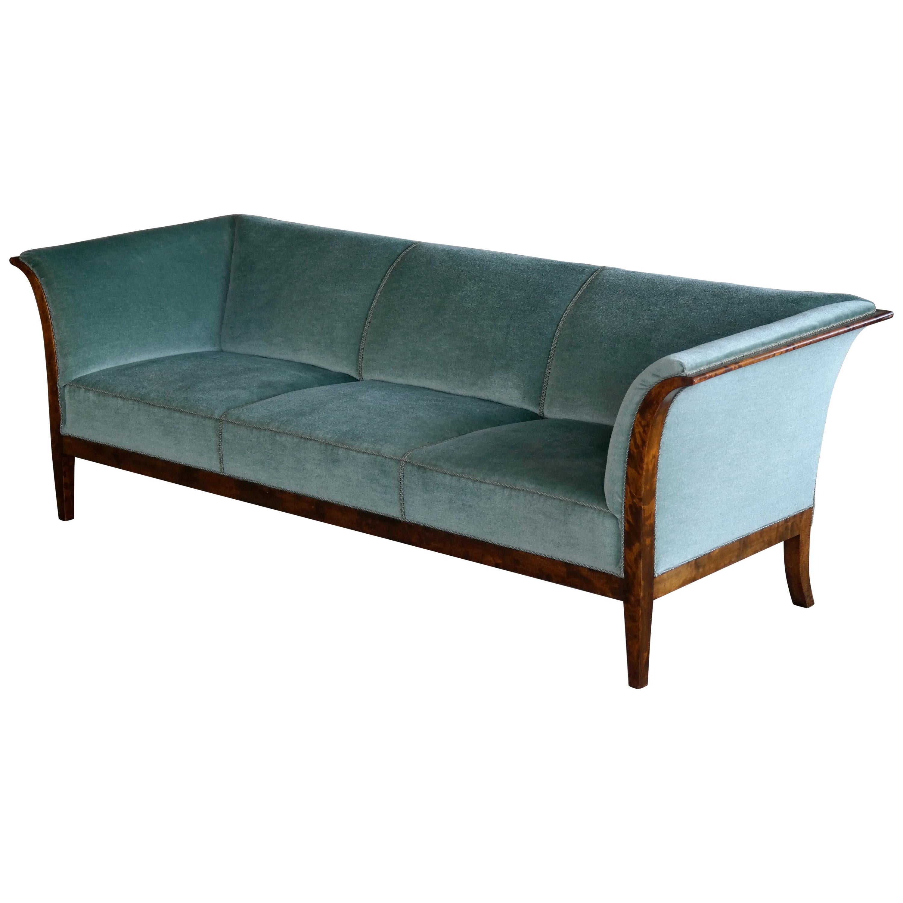 This elegant and generously sized three-seat sofa was designed and made by the Danish Master Cabinetmaker, Frits Henningsen in 1938. Constructed from beautiful flamed birch wood the frame extends from flared armrests and into tapered front legs.