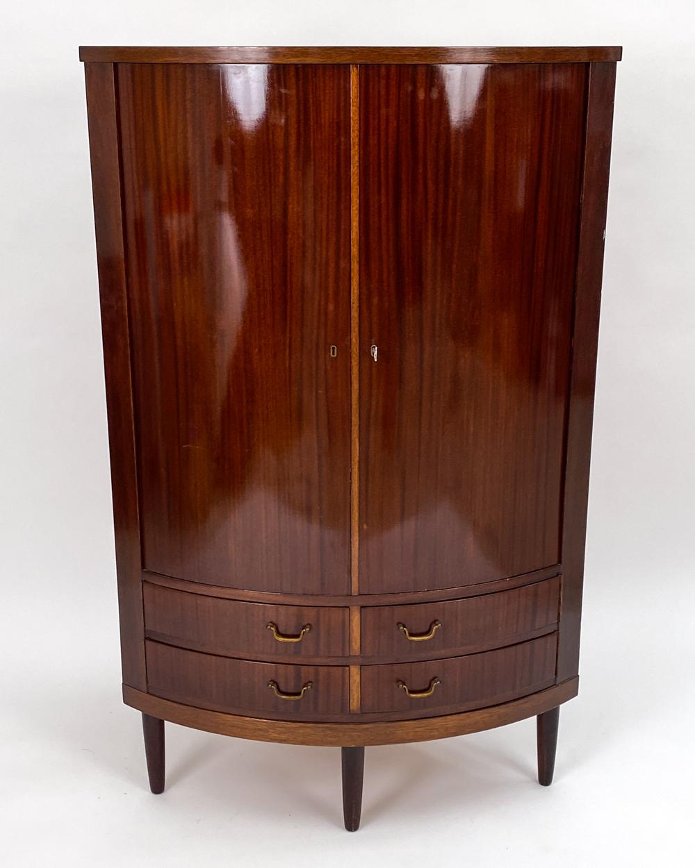 A handsome Danish mid-century corner cabinet with a rounded front, in the manner of Frits Henningsen's traditional-leaning designs. In rich, beautifully grained mahogany, this cabinet oozes elegance. c. 1960's. Including key.