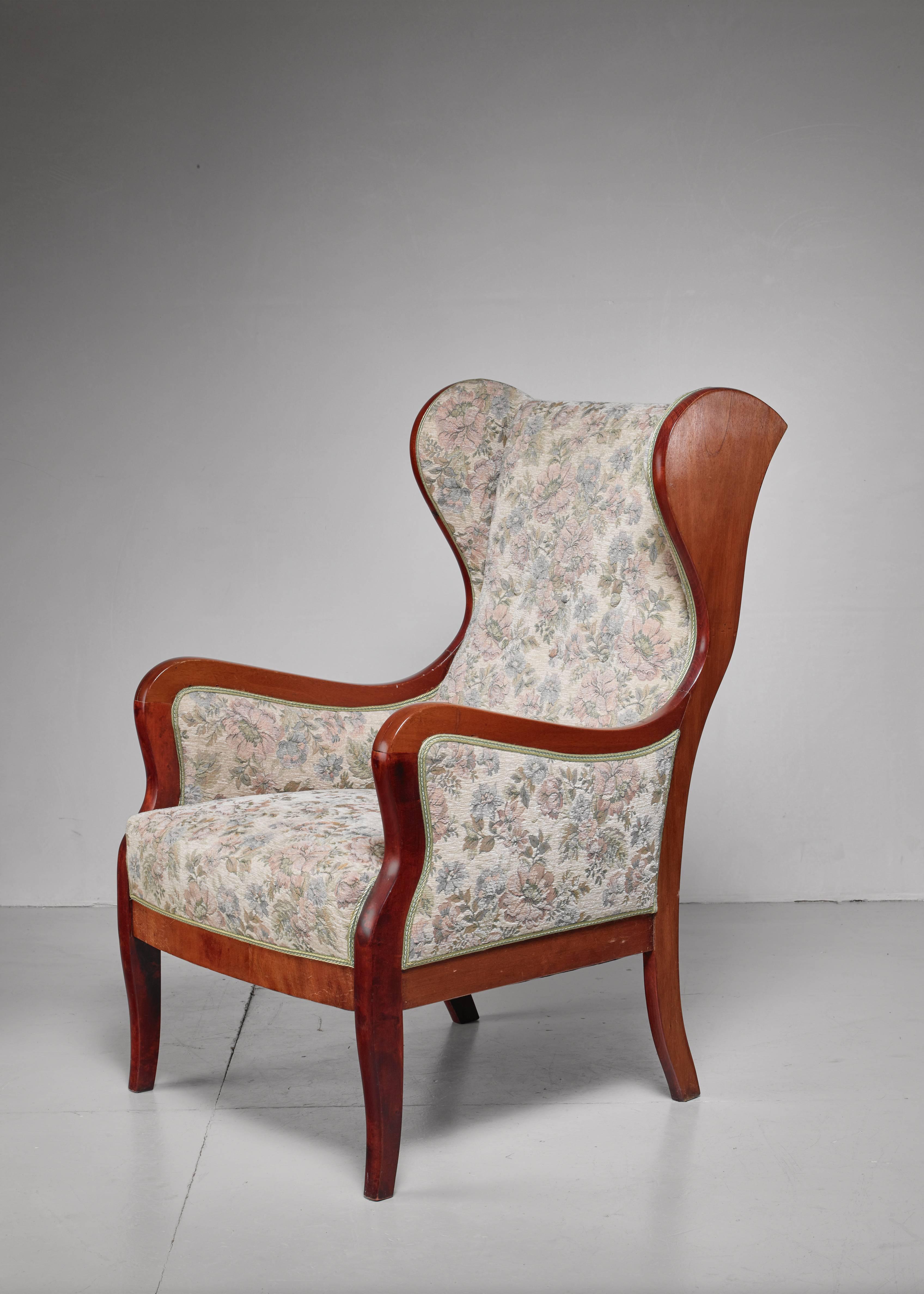 An elegant and comfortable mahogany wingback lounge chair with original floral fabric upholstery, by Frits Henningsen.

The elegant construction of the mahogany frame and curved back is a great example of Henningsen's craftsmanship. 

We can