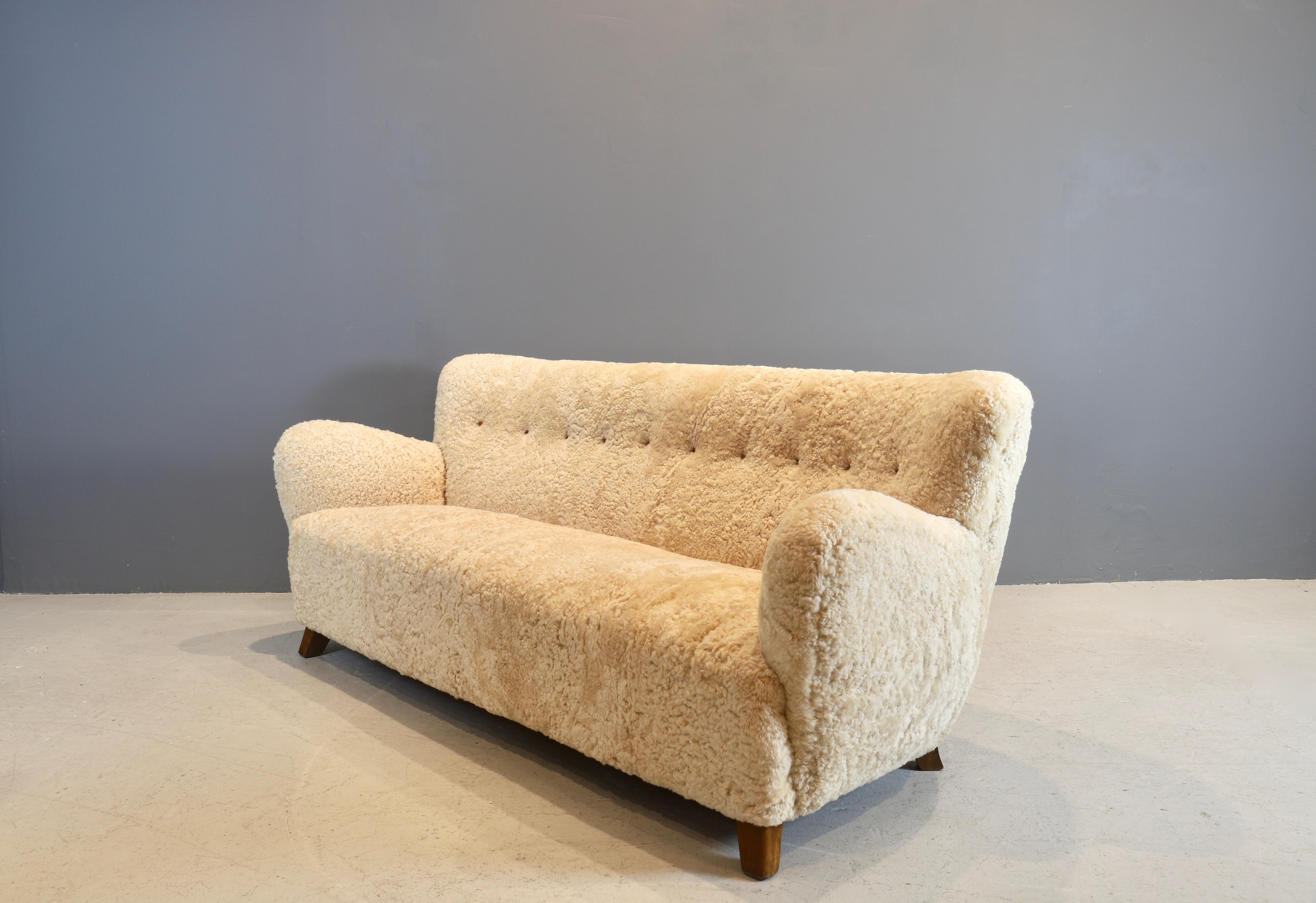 Vintage Fritz Hansen couch, circa 1940s masterfully reupholstered in light beige shearling with leather buttons. Oak legs have been cleaned and oiled.
This couch is available to view in the gallery.