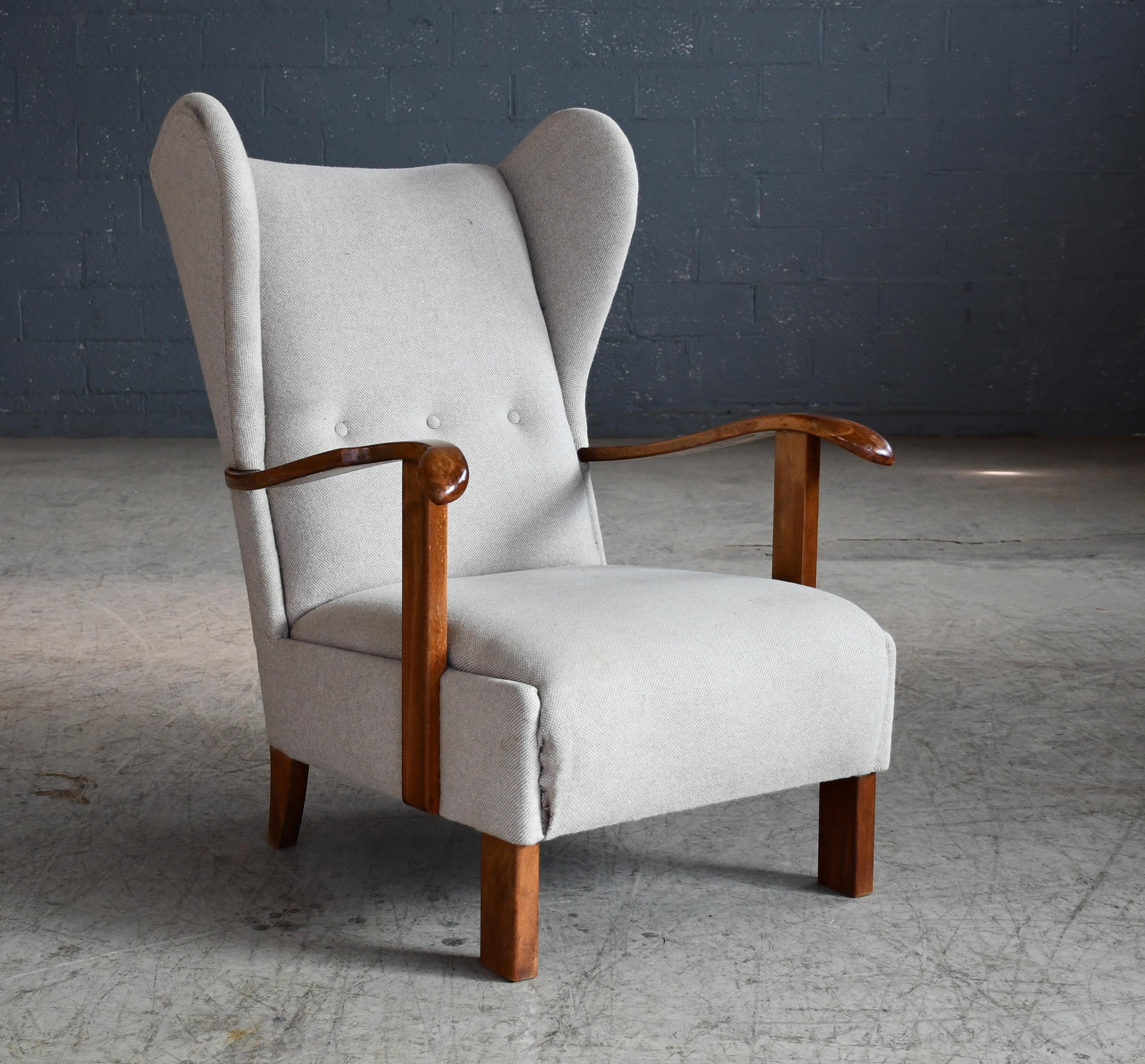 Very cool low swung wing back lounge chair made by Fritz Hansen in Copenhagen, Denmark as model 1582. The wooden armrests and legs are made of varnished oak wood showing great grain and patina and just minor natural wear. The chair was seen in the