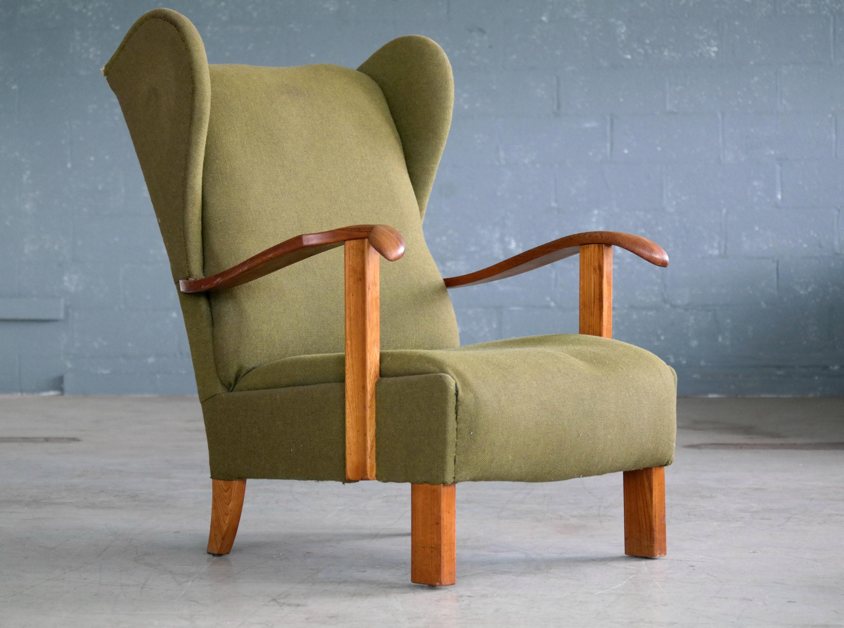 Very cool low swung wing back lounge chair made by Fritz Hansen in Copenhagen, Denmark. The wooden armrests and legs are made of varnished beech wood showing great grain and patina and just minor natural wear. The chair still has the handwritten ink