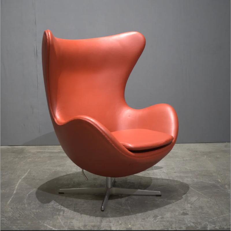 The Orange Leather Egg Chair by Fritz Hansen is an iconic piece of mid-century modern design, exuding elegance and style. Designed by Arne Jacobsen in the 1960s, this chair is upholstered in luxurious orange leather, making it a striking statement