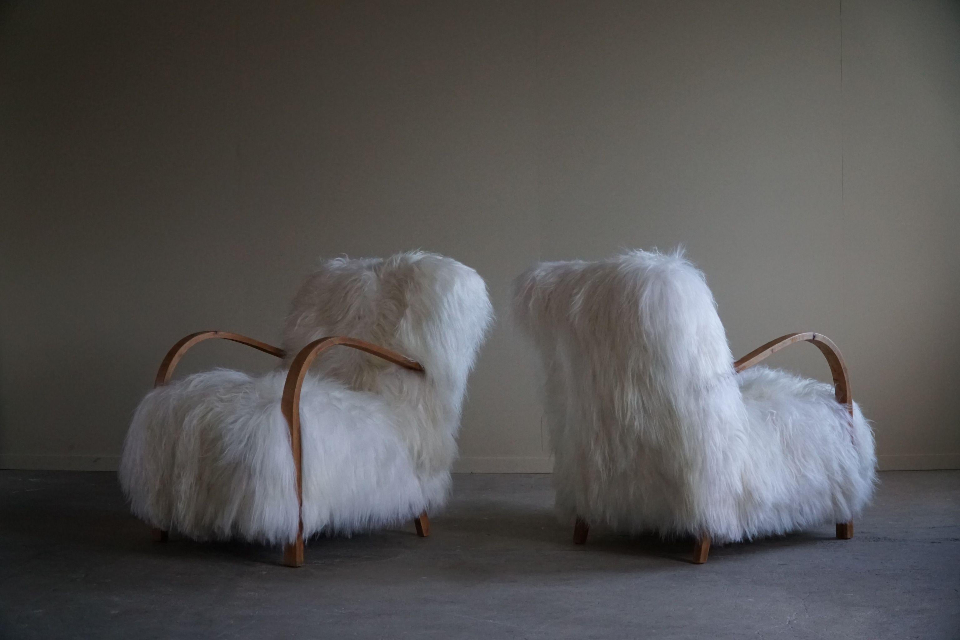 Ein so exquisites und seltenes Paar Art Deco Sessel mit Armlehnen aus massiver Eiche. Die Stühle wurden fachmännisch mit einem luxuriösen isländischen Schaffell gepolstert, das der Gesamtästhetik eine weiche und fühlbare Textur verleiht. Die Wolle