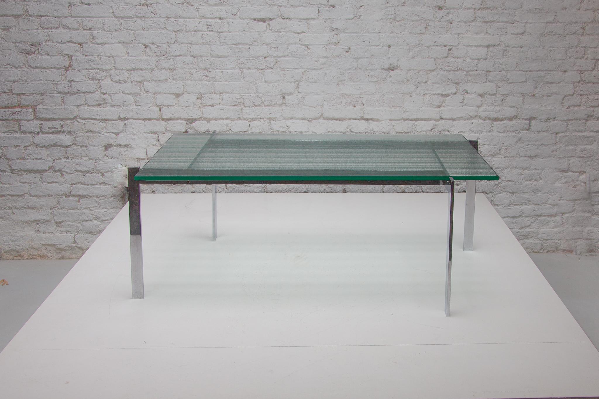 Table au design minimaliste dotée d'une structure originale en acier inoxydable et d'un plateau en verre transparent à structure en ruban. Les quatre éléments de la base sont assemblés par des vis mécaniques qui donnent à la table son aspect unique.