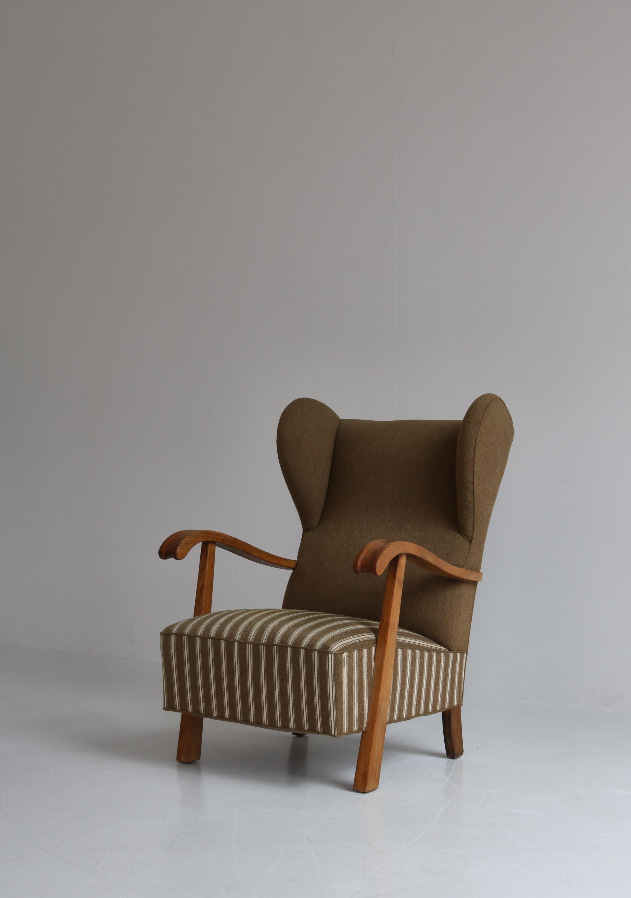 Large and sturdy 1940s wingback lounge chair attributed to Fritz Hansen, Copenhagen. Beautiful Danish design with wonderful sculpted armrests in solid patinated oak. The chair is upholstered in seat and back with iron spring cushions in Savak