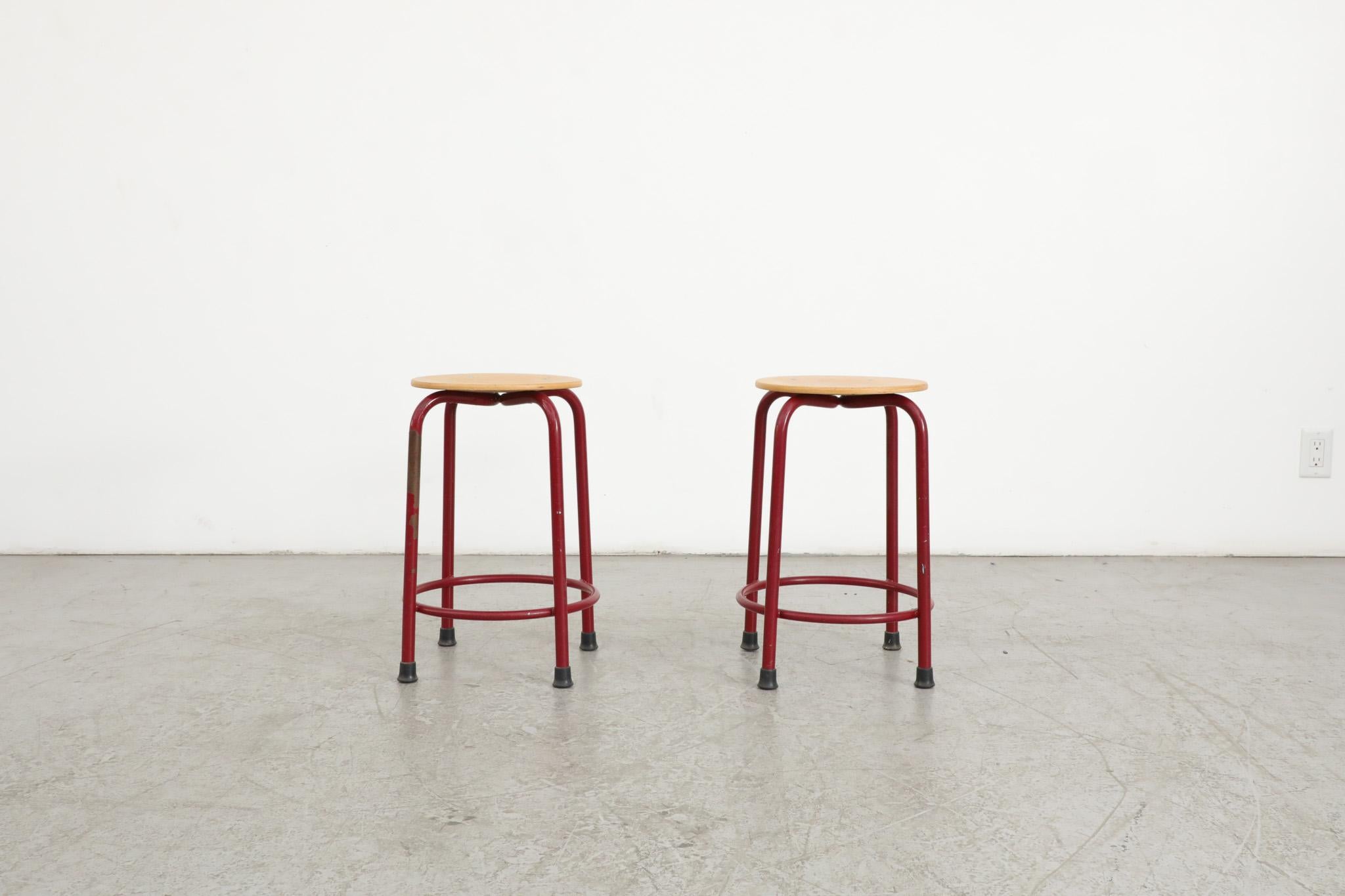 Mid-Century, Fritz Hansen style industrial task stools with red enameled metal frames and well loved blonde wood seats. The seat height is 20.25