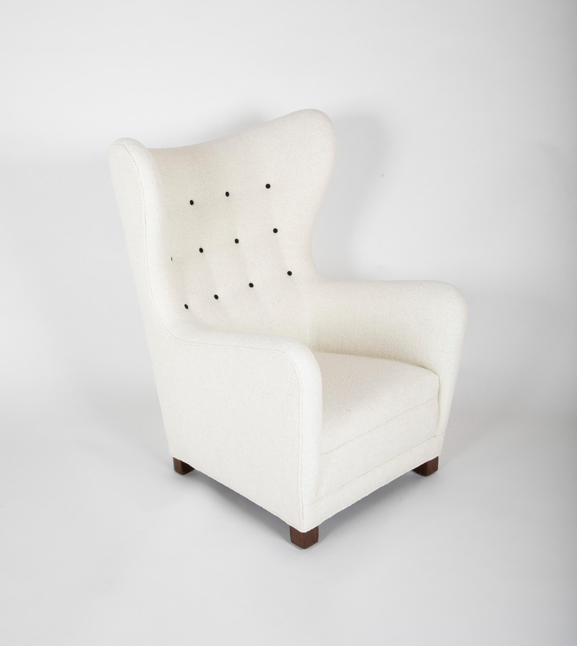 Wing chair model FH 1672, produced by Fritz Hansen during the 1940s. This armchair, with voluptuous curves, newly upholstered in Boucle fabric with black buttons and rests on walnut stained beech base.