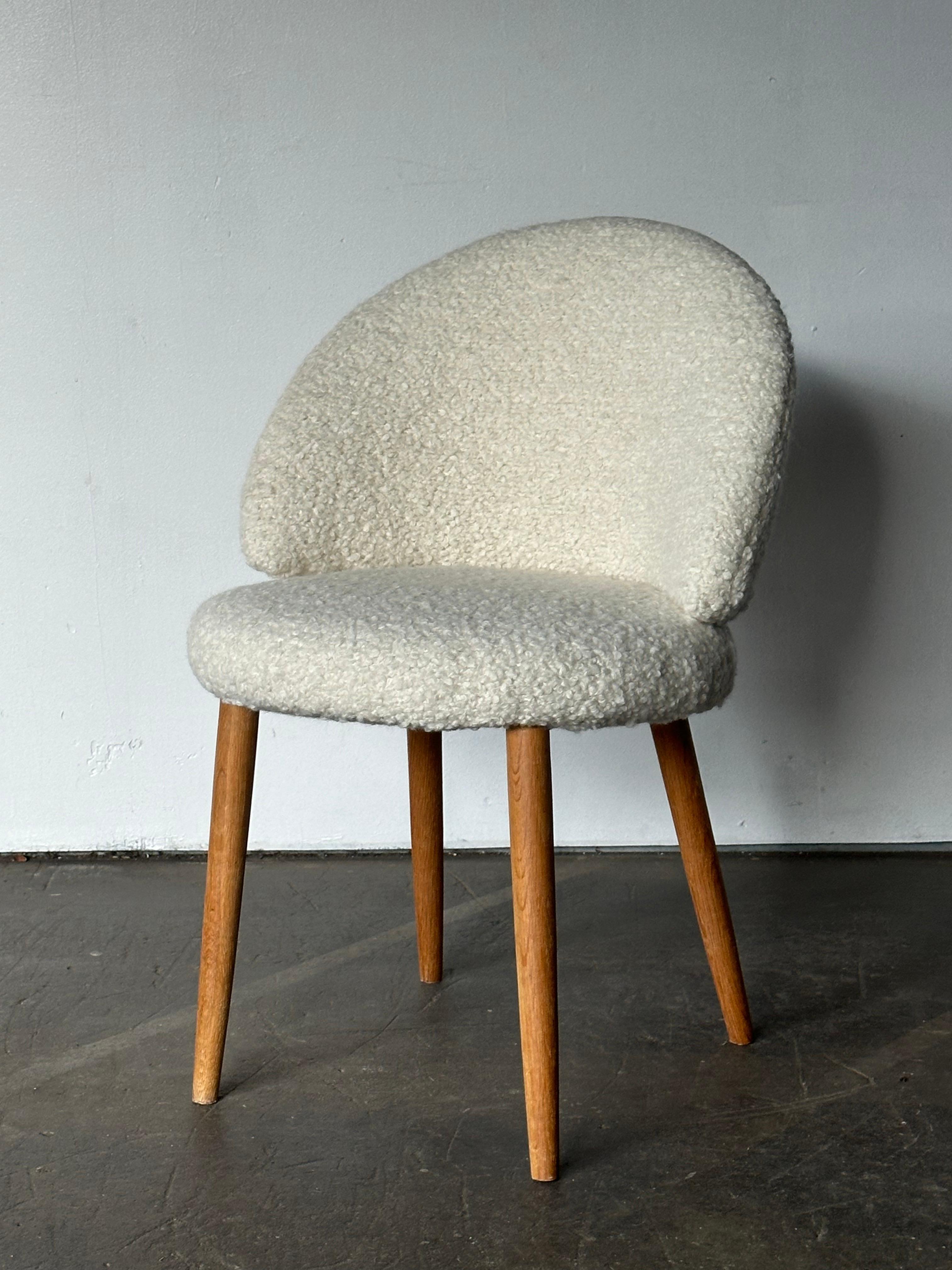 Bellissima ed elegante poltrona da toilette di piccole dimensioni disegnata da Frode Holm. Realizzata in un nuovo tessuto bouclé color crema, con una comoda seduta e uno schienale in schiuma di sostegno e gambe in legno massiccio biondo con finitura