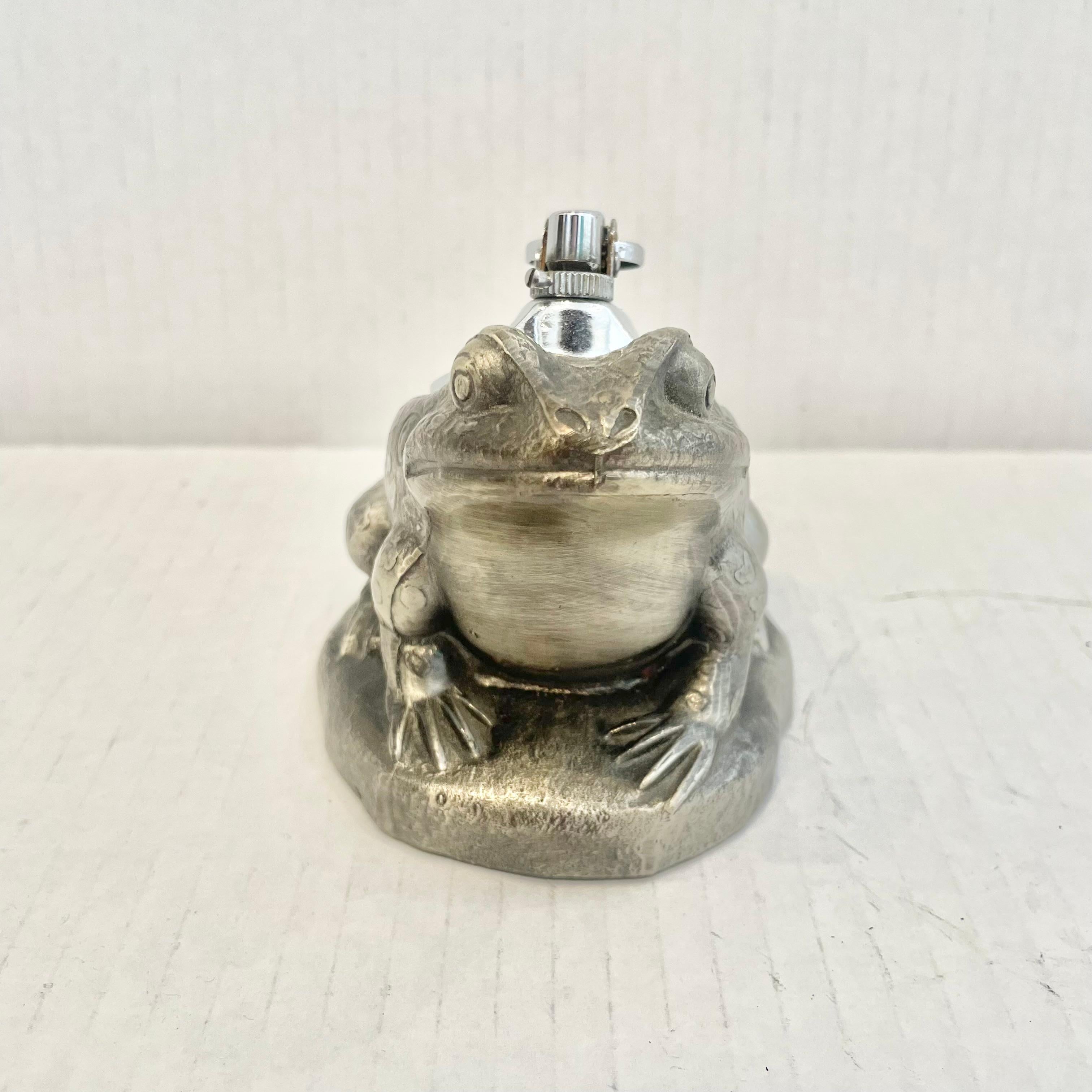 Cool vintage table lighter in the shape of a seated frog. Made completely of metal with a hollow body. Beautiful silver color with details like small spots all over the frogs bogs. Cool tobacco accessory and conversation piece. Working lighter. Very