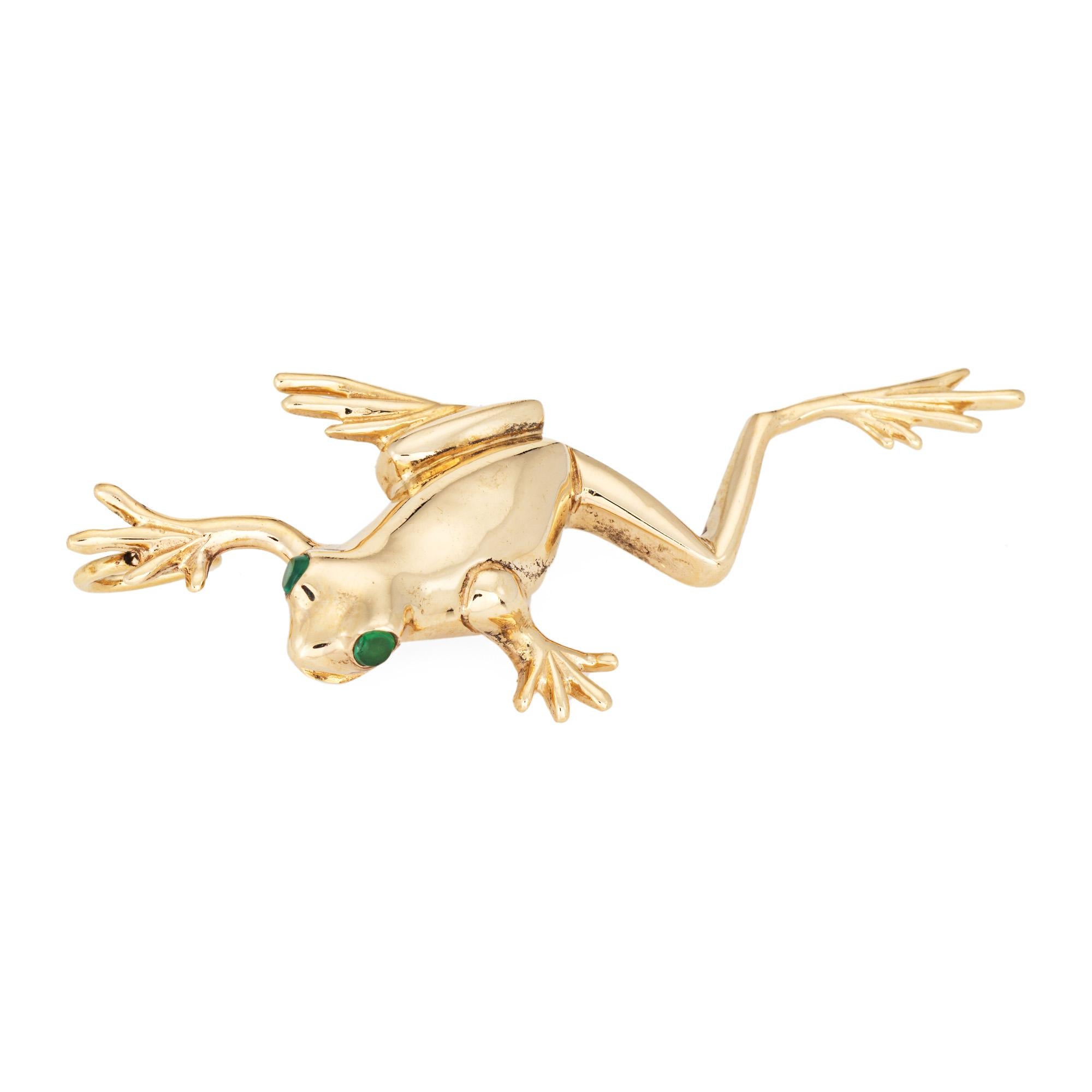 Pendentif grenouille finement détaillé en or jaune 14 carats. 

Deux petites émeraudes estimées à 0.02 carat sont serties dans les yeux.

La grenouille magnifiquement détaillée est conçue comme si elle était en mouvement. Ce pendentif poli est idéal