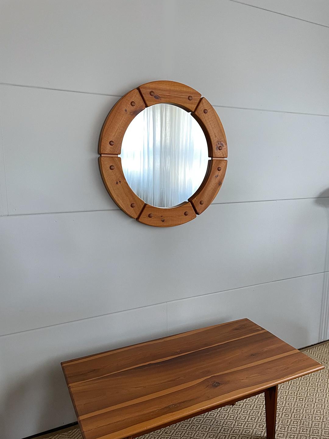 Sculptural round mirror with solid pine wood frame made by Fröseke AB Nybofabriken from the 1960s, Sweden. Massive frame with decorative wooden nails. Stamped: Made in Sweden. The mirror is in very good condition. 
We love to create the illusion of