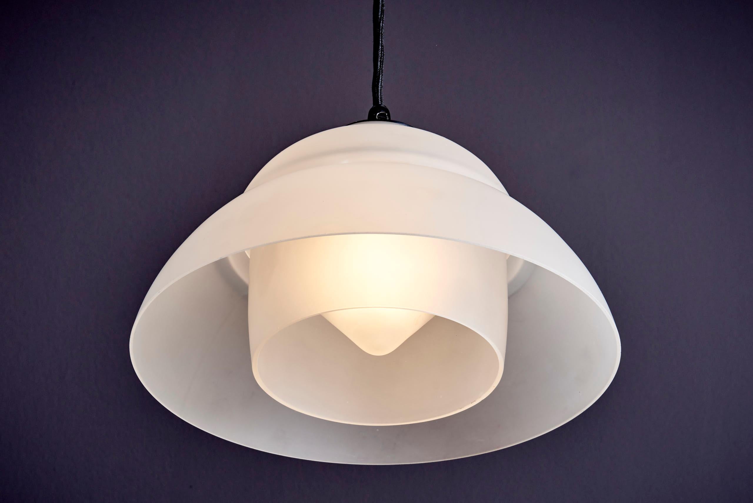 Lampe suspendue en verre dépoli des années 1930. Elle est dotée d'un abat-jour en verre stratifié en deux parties qui diffuse une lumière douce et homogène. Le design incurvé crée un look simple et élégant. Vintage By avec une légère usure due à