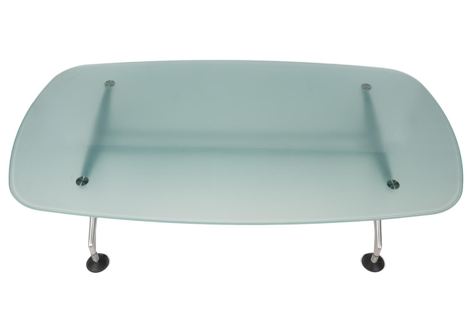 This modern coffee table designed by Antonio Citterio for Vitra, Germany features a slightly curved rectangle made of tempered frosted and slightly colored glass resting on a brushed metal support with four angled legs ending in circular pad feet.