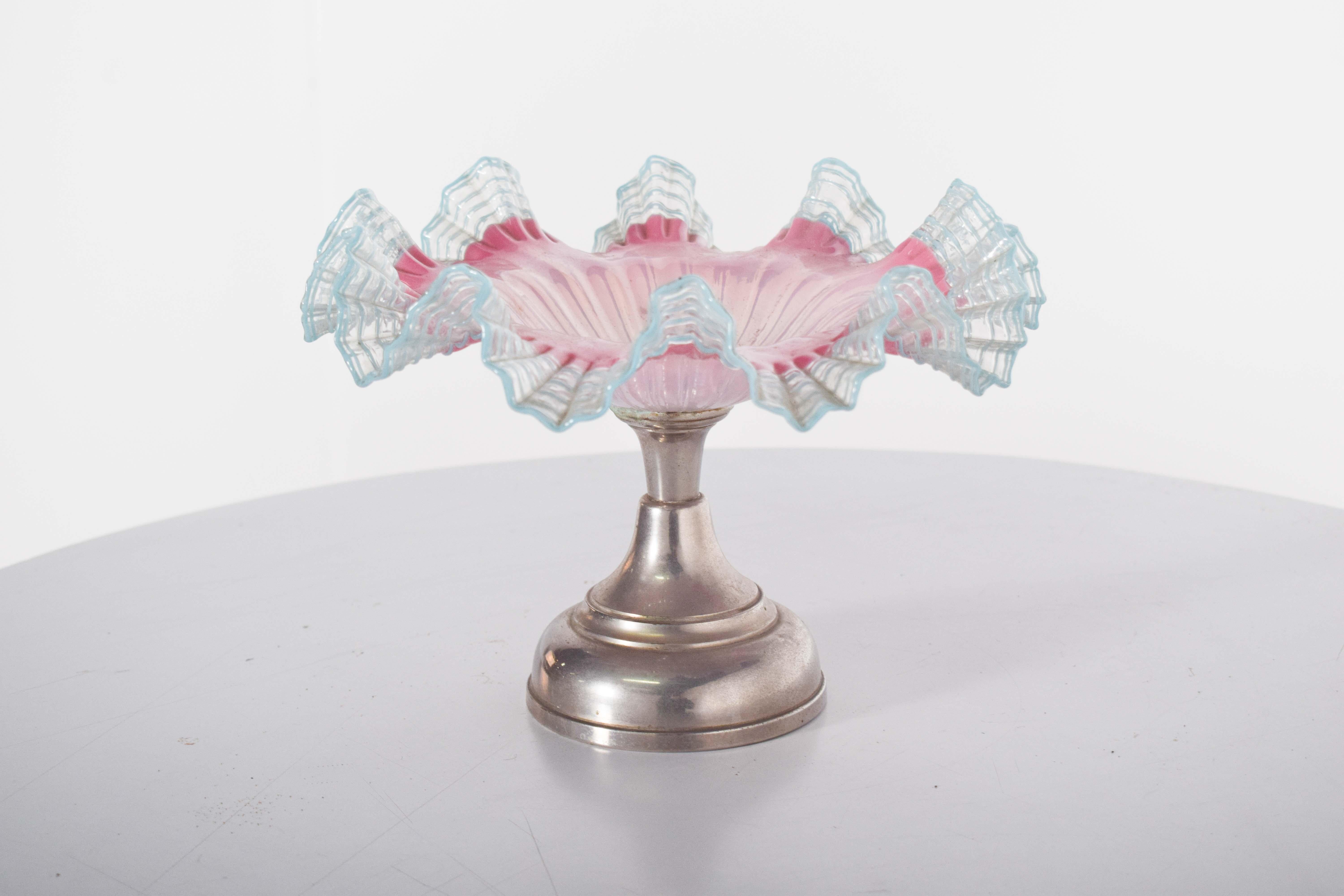Fruit bowl in glass and metal. Silver metal base, with a rounded and slightly concave shape, providing stability and support to the structure. The central stem, also metallic, features a turned shape, with smooth transitions and a polished finish