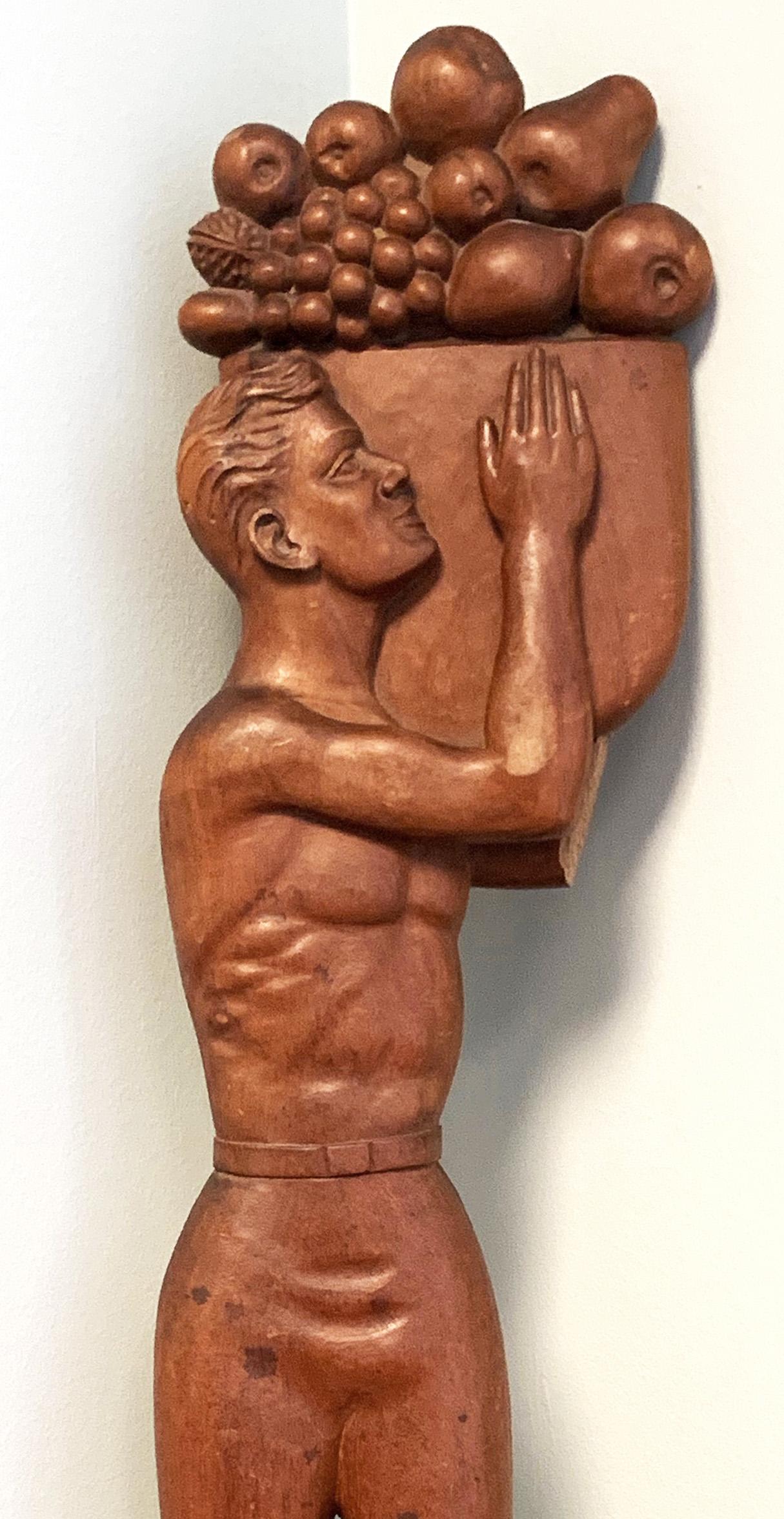 Large and impressive, carved in a naive-sophisticated way that suggests folk art as well as WPA sculptures which glorified the worker, this large bas relief depicts a shirtless young man carrying a large basket overflowing with grapes, apples, pears