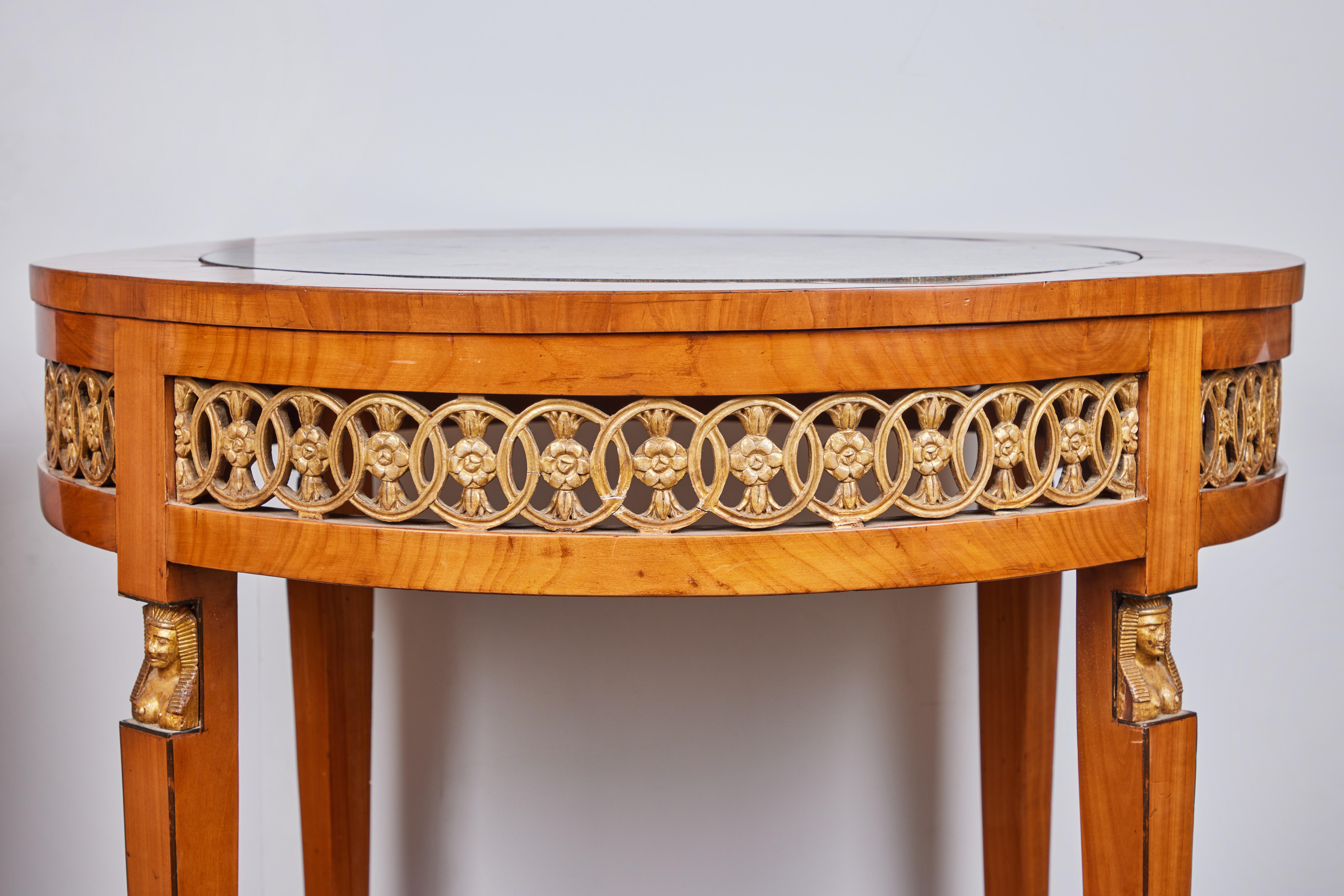 An elegant hand carved round table with inset marble top. The intricate carving in the apron is gilded as is the carved Pharaohs head and feet. The column legs have ebonized trim and the bun feet are ebonized.

