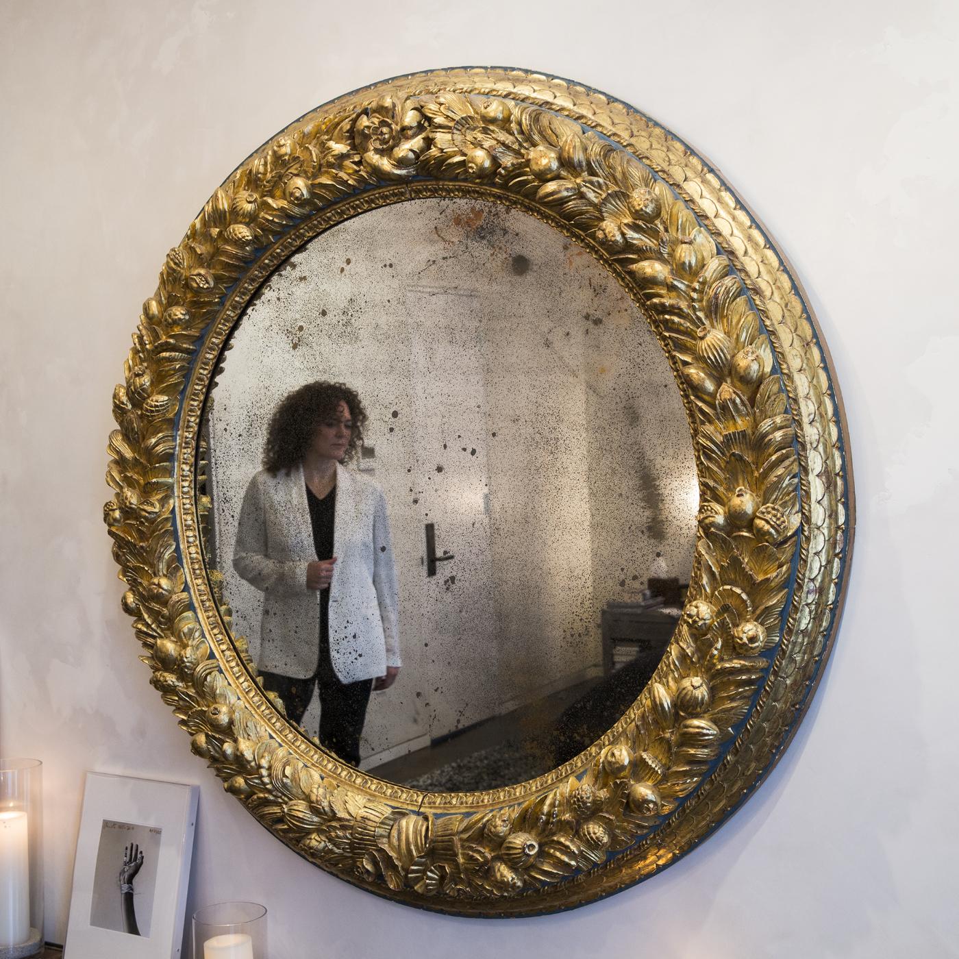 This is a hand-carved round pinewood mirror by Daniele Nencioni, finished with pure gold leaf. The piece is decorated in the stunning Robianna style with fruit and leaves, making it a fascinatingly refined ornament. It comes with a mirror with an