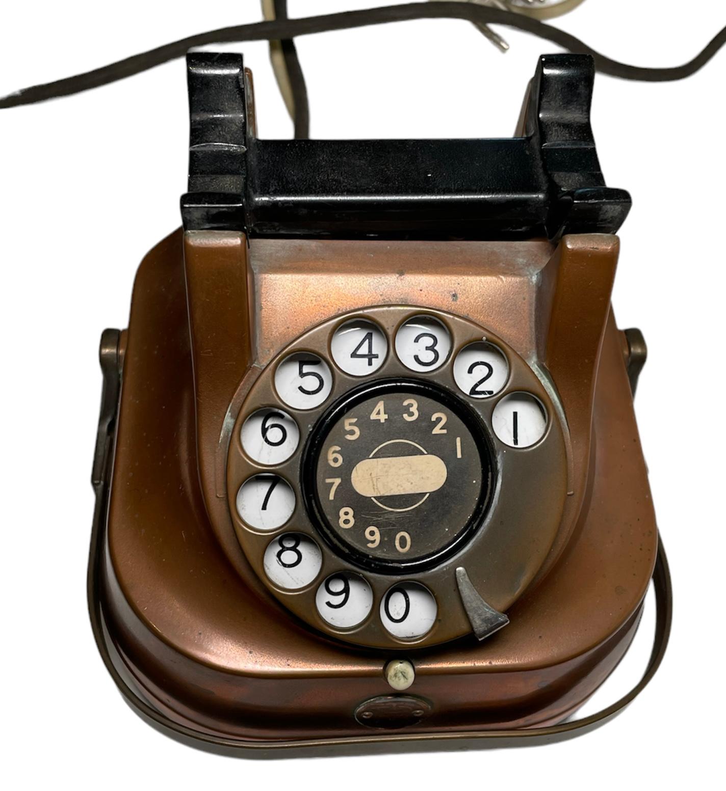 This is a FTR table rotary dial telephone. It’s case is made of copper and the handset is made of Bakelite. The rotary dial and handle are made of brass. There is a round small metal plaque hallmarked FTR in the front of the telephone. Two cords