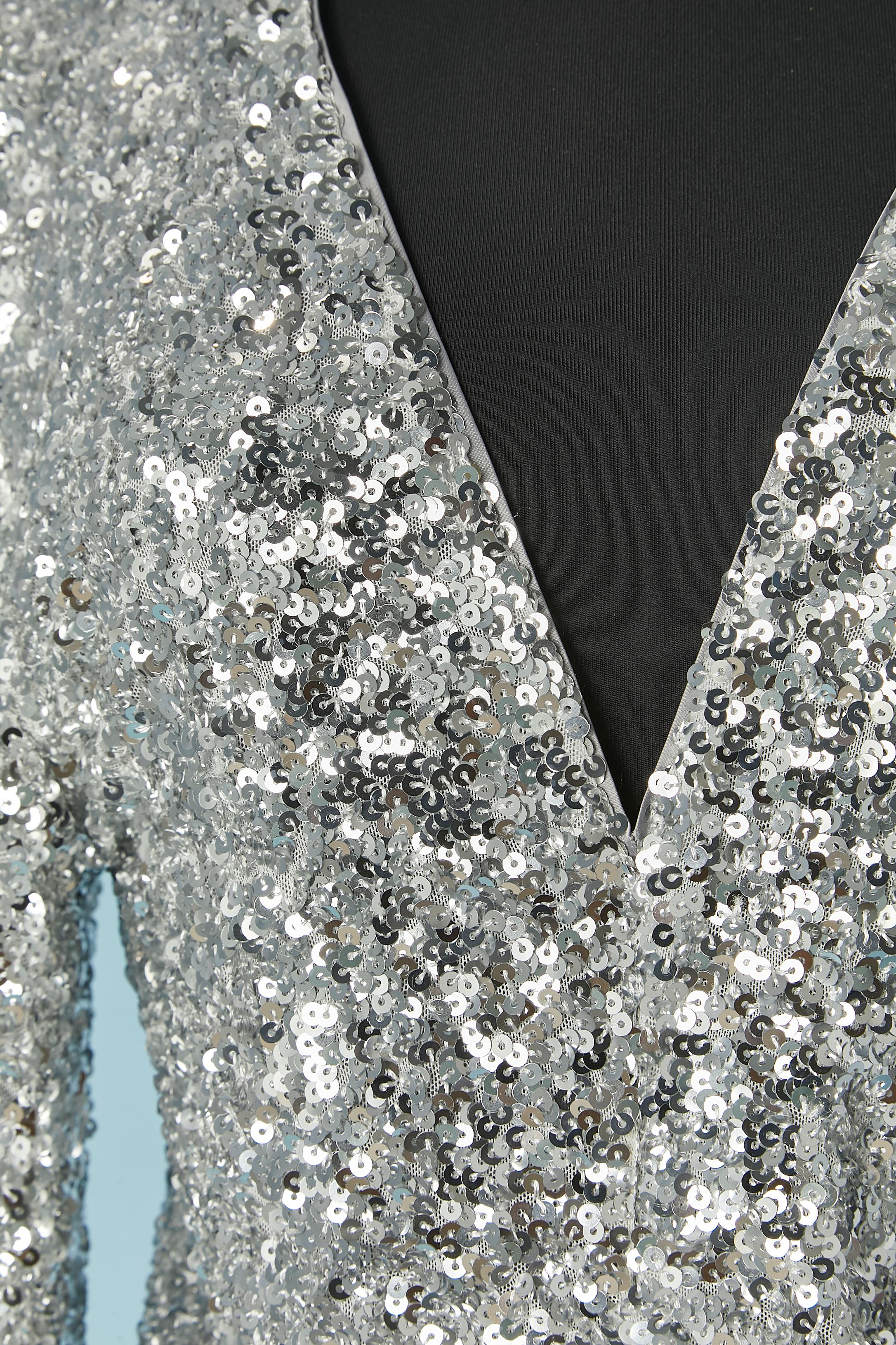 Tuta intera in paillettes argento con maniche a palloncino. Tessuto principale: 95% poliestere, 5% elastan. Fodera: 95% poliestere jersey, 5% elasticizzato 
Chiusura con zip e gancio al centro della schiena. Drappeggiato sulla parte anteriore