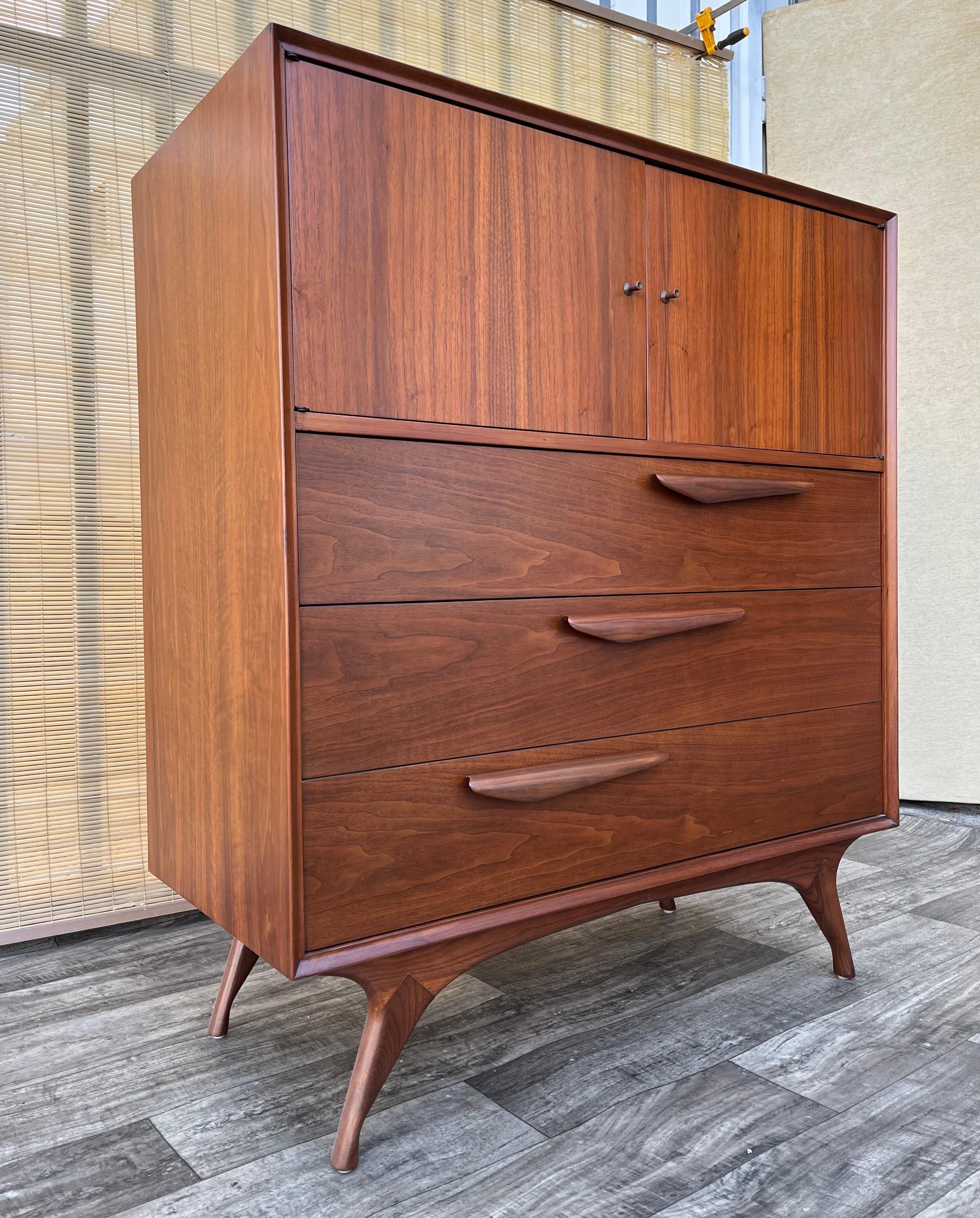 Comò Highboy scolpito d'epoca completamente rifinito in stile Mid Century Modern. Circa anni '60
Presenta un bellissimo design scolpito in stile Mid Century Modern, con gambe ricurve, una splendida venatura del legno di noce, cassetti con tiretti