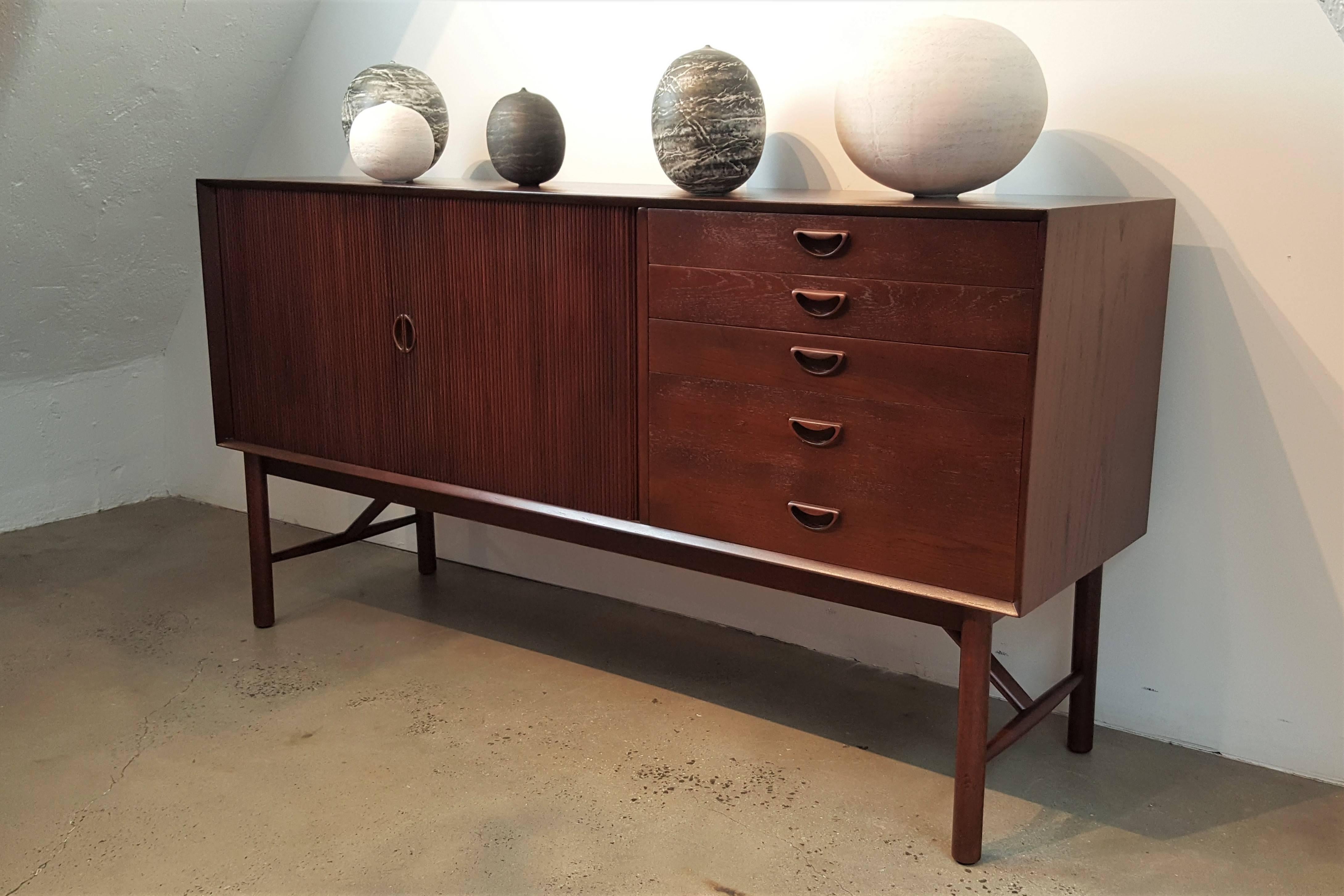 Fully restored teak buffet or credenza designed by Peter Hvidt. Extremely functional, versatile piece of Danish Modern midcentury design. Sculptural, integrated handles and pulls with tambour doors. Top drawer is divided and lined for silver.
This